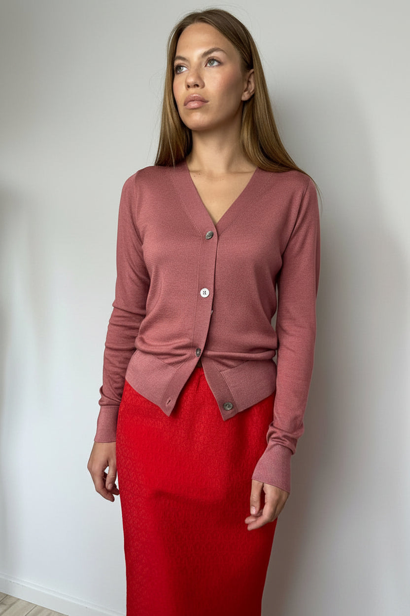 Woman wearing a pink cardigan and red skirt against a white wall.