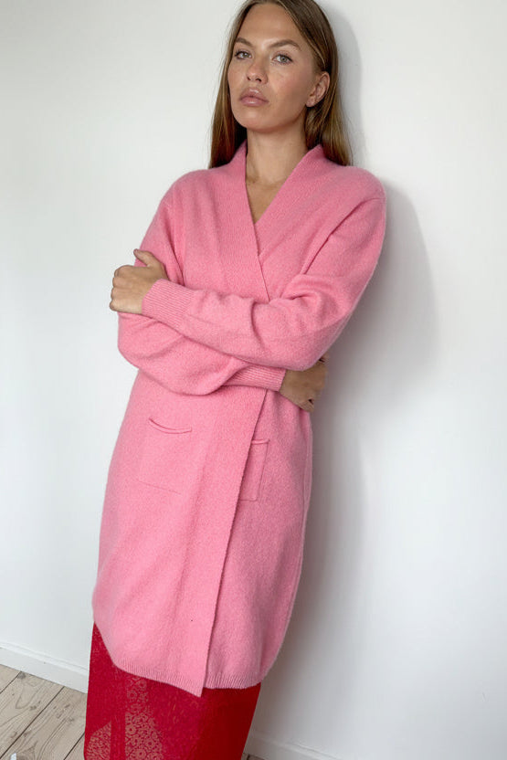 Woman wearing a pink robe against a white wall