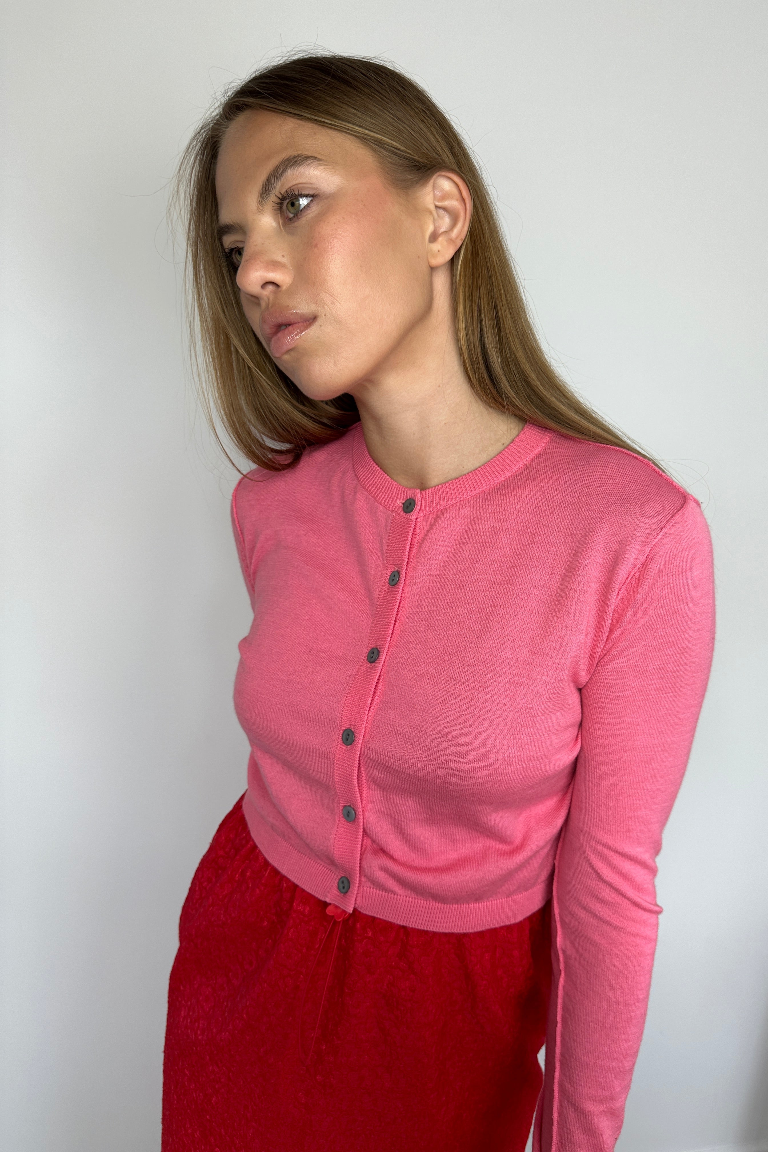 Person wearing a pink top with buttons and red pants on a white background