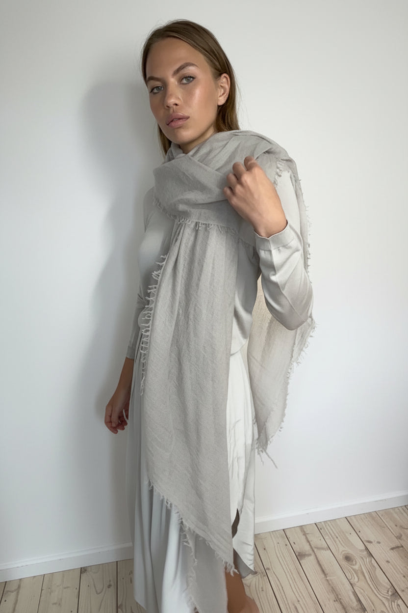 Woman wearing a light gray scarf against a white wall.