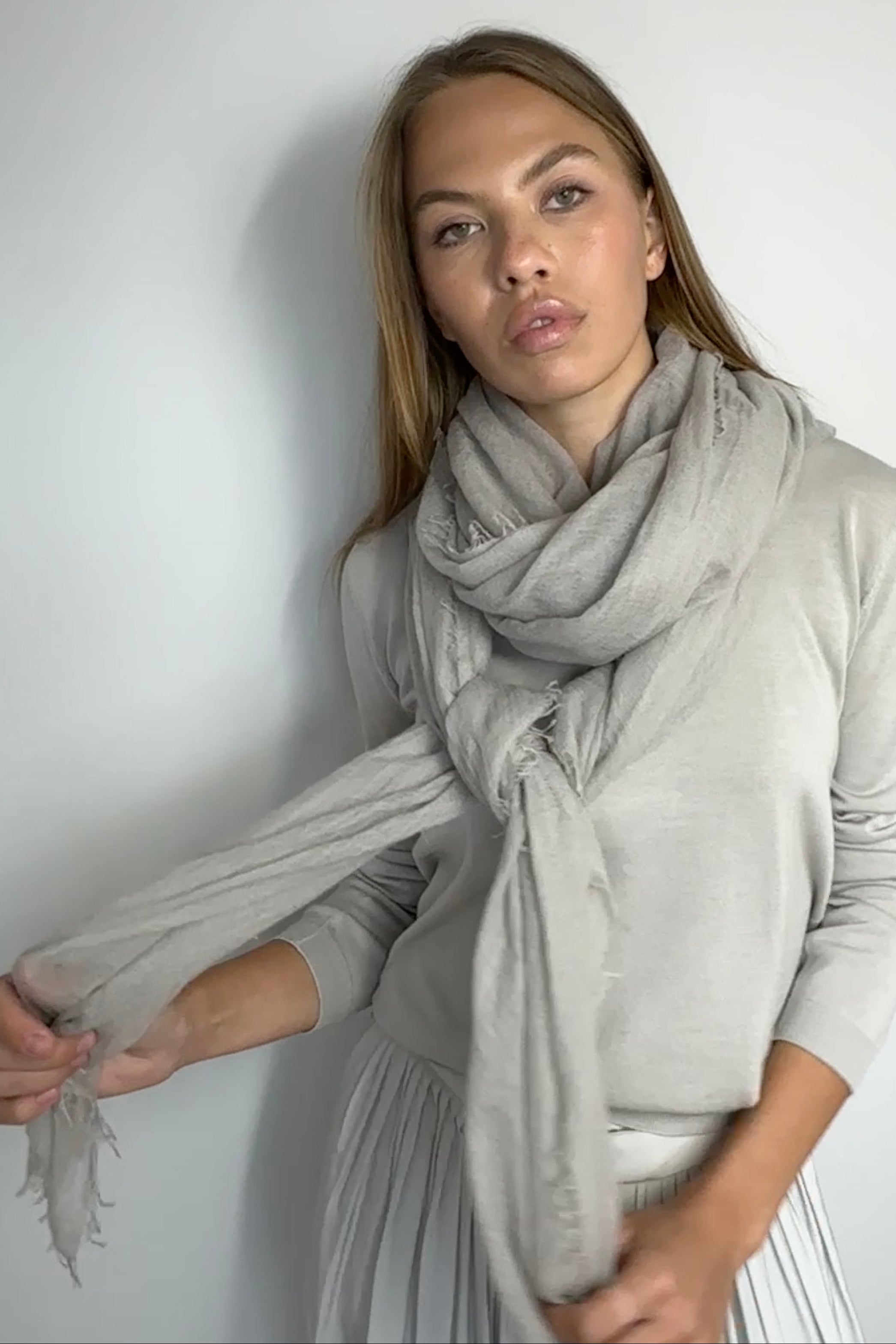Woman wearing a light gray scarf against a white wall