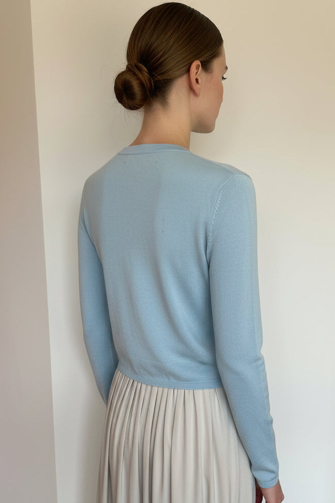 model wearing a light blue sweater and white skirt against a plain background