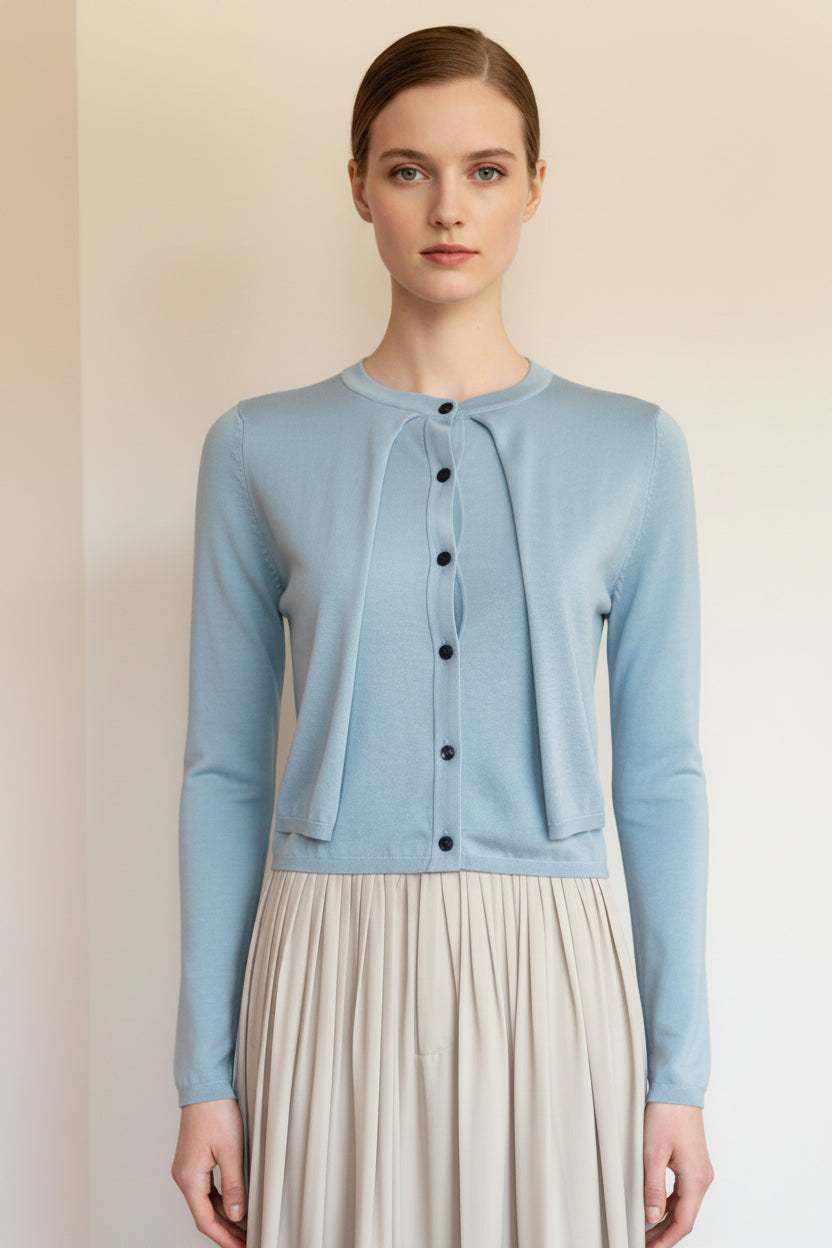 Woman wearing a light blue cardigan over a beige dress against a plain background