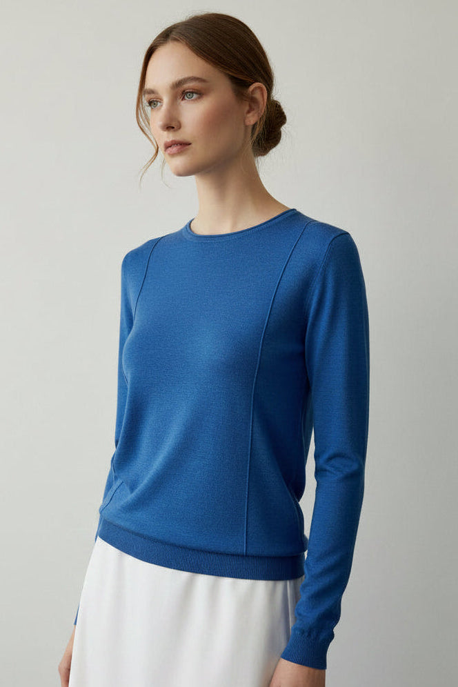 Woman wearing a blue sweater and beige pleated skirt on a light gray background