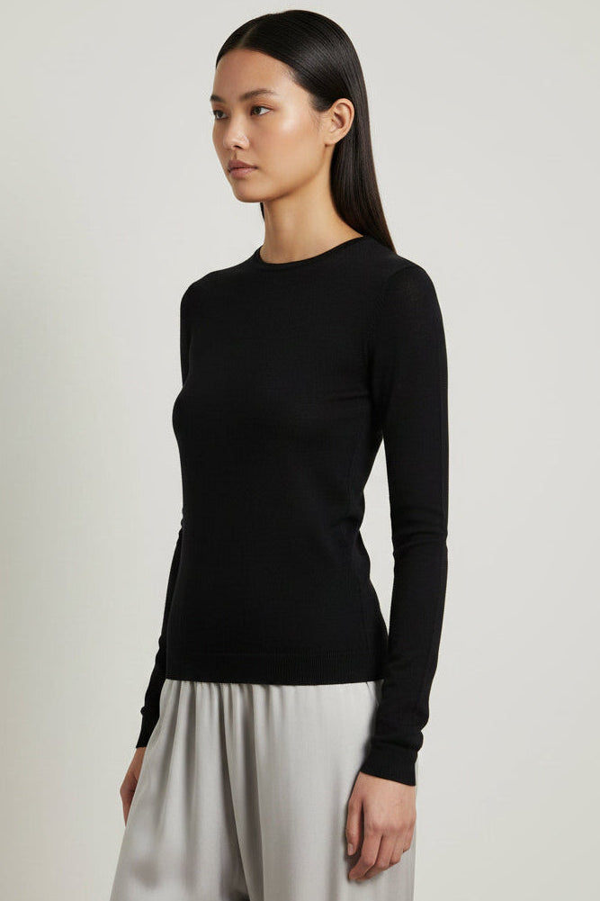 Model wearing a black long-sleeve top and beige skirt against a plain wall.