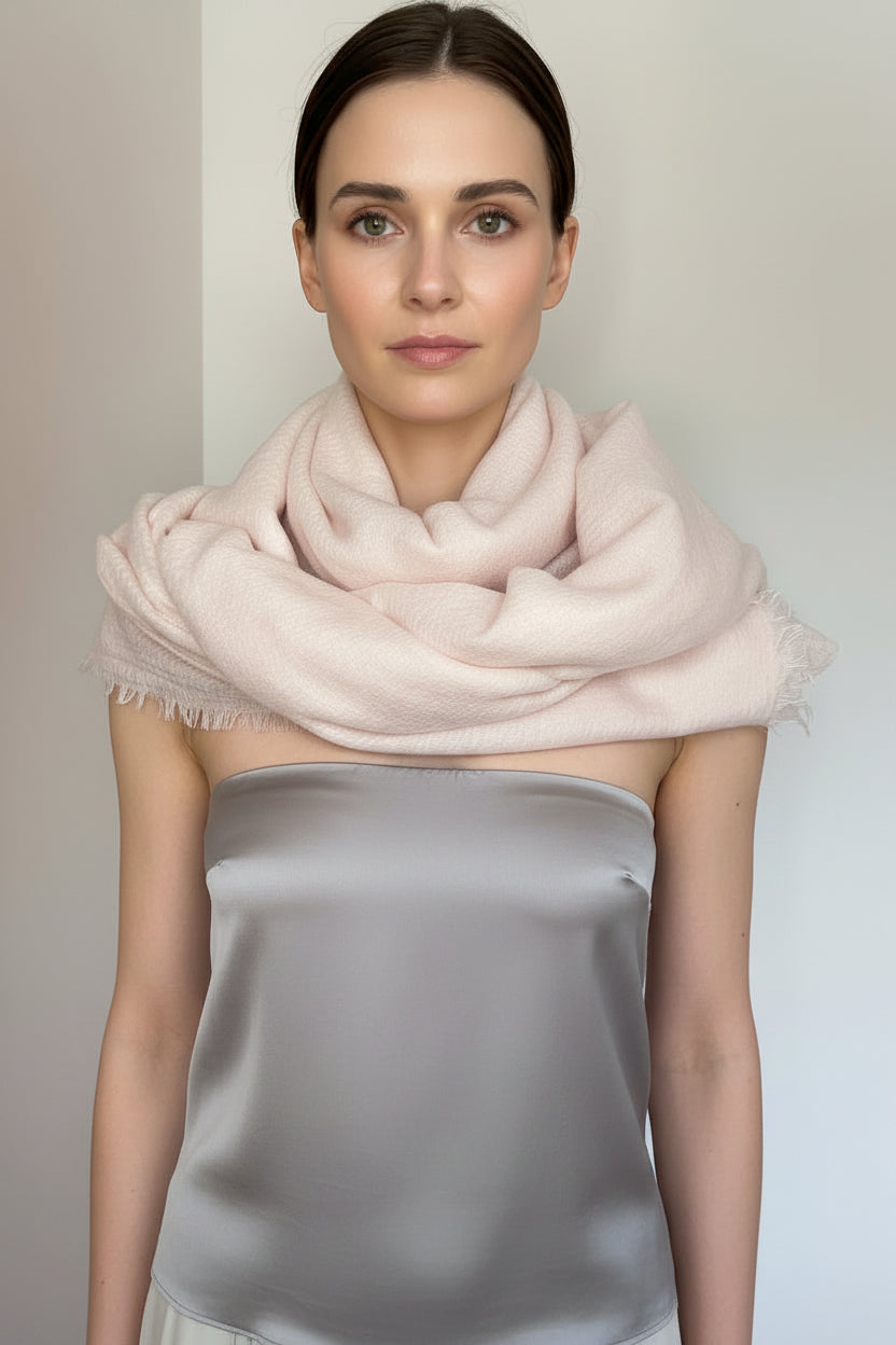 Woman wearing a light pink scarf and light gray outfit against a plain background