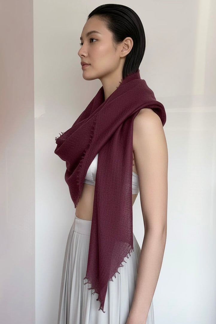 Woman wearing a maroon scarf and white dress against a plain background