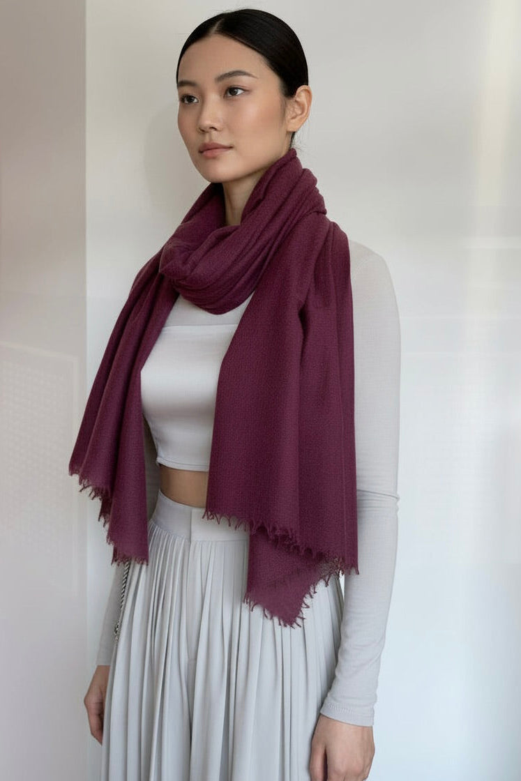 Woman wearing a purple scarf over a white top and light gray cardigan against a plain background