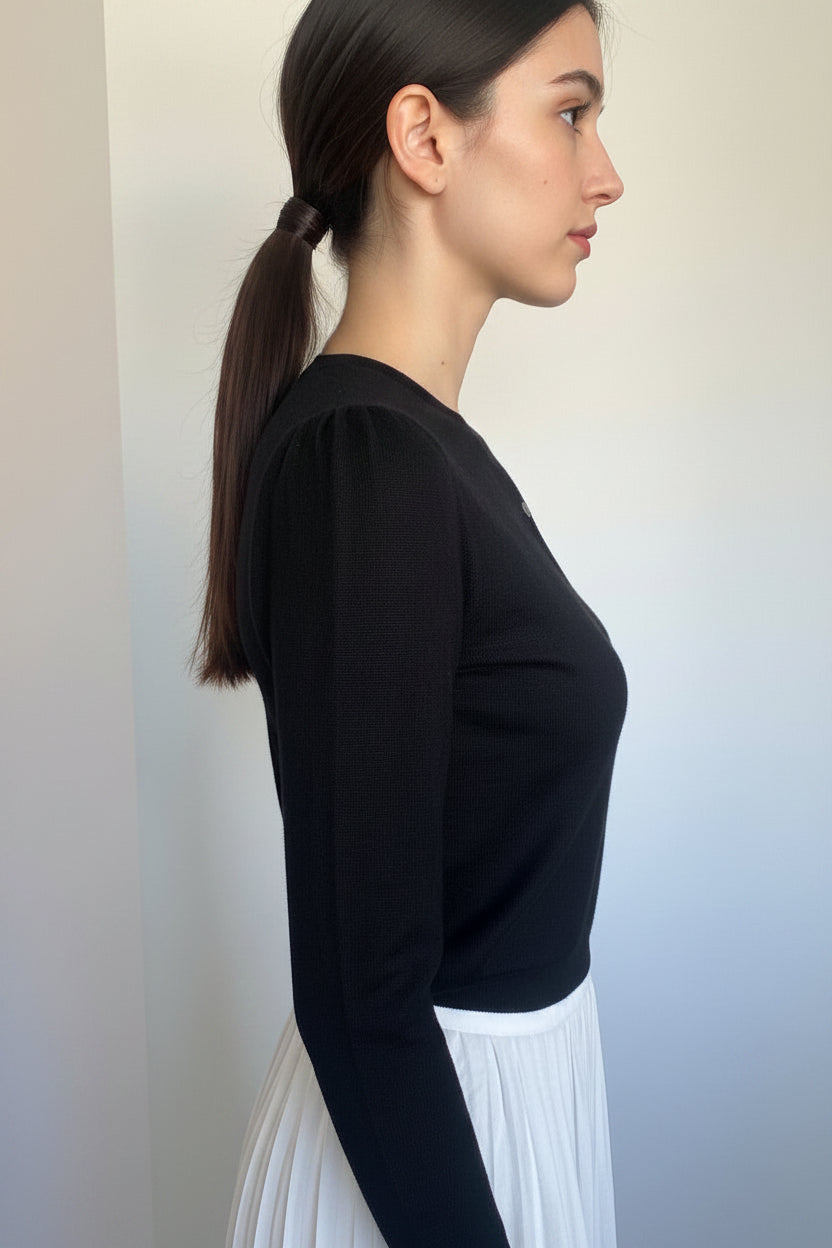 A black knit long-sleeve top displayed on a  model from a side profile view against a plain indoor wall.
