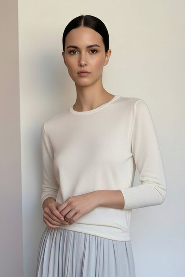 A cream-colored long-sleeve knit top displayed on a white mannequin, paired with a light gray pleated skirt, set against a plain indoor wall.