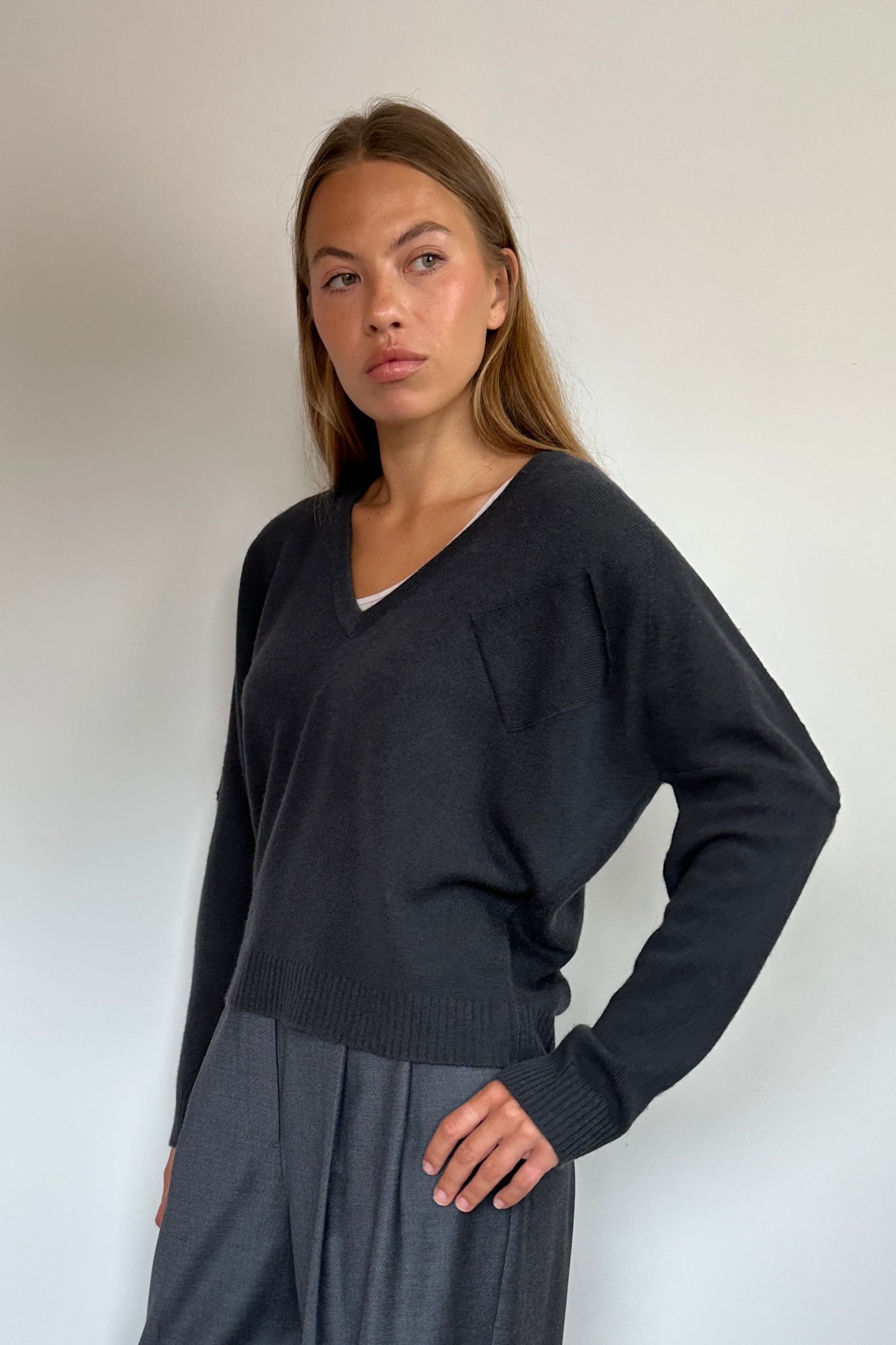 A woman modeling a dark charcoal gray knit sweater and matching wide-leg trousers, standing against a plain white wall on a light wood floor.
