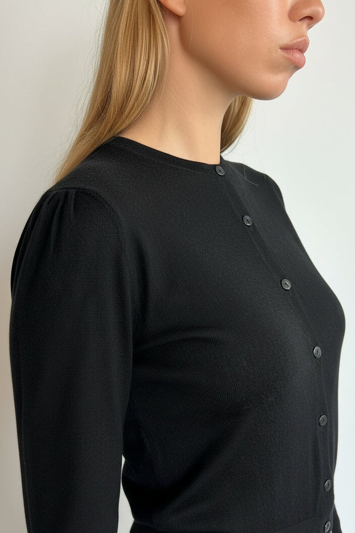 A woman wearing a black long-sleeve button-up top, shown in a side profile view against a plain light background.