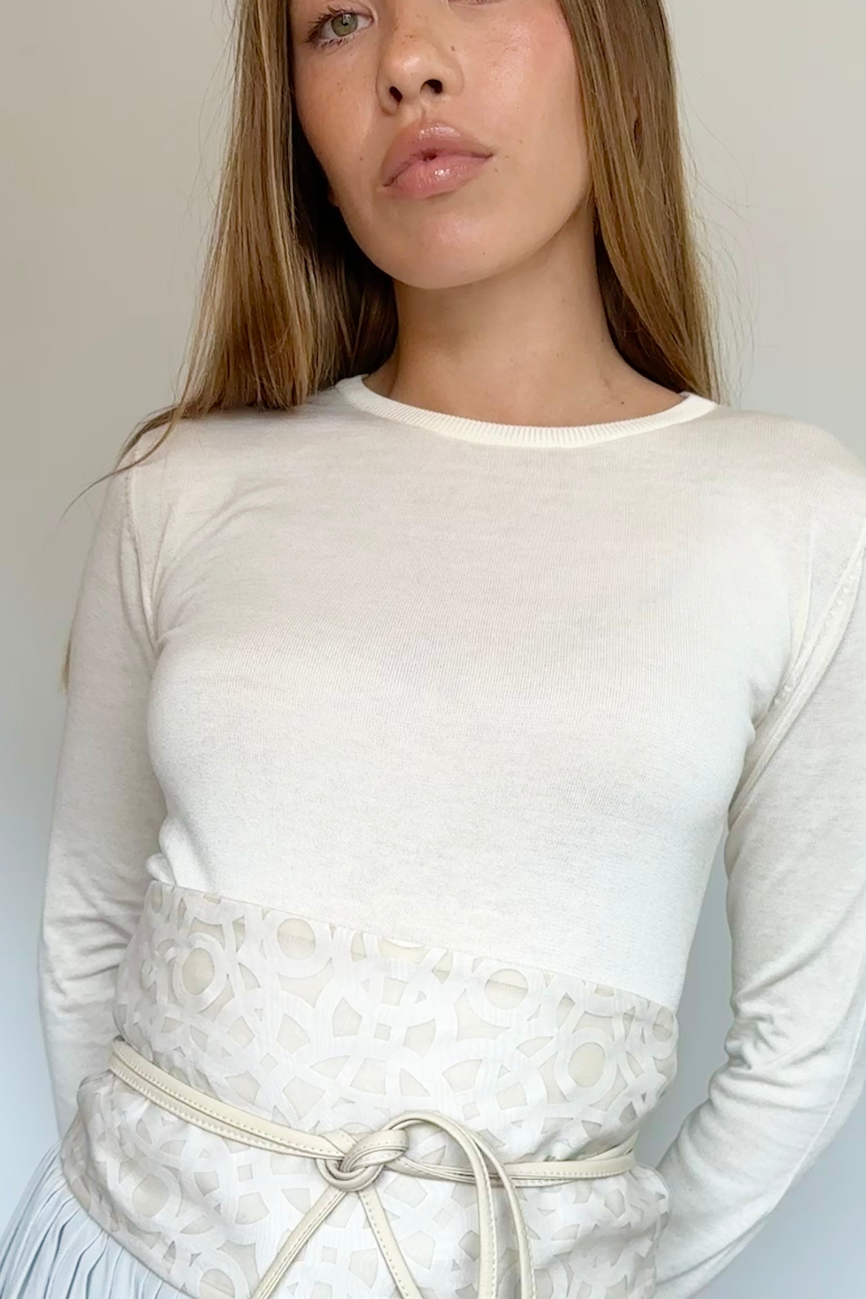 A woman wearing a fitted long-sleeve cream top with a textured waist panel and a matching drawstring belt, shown against a plain light background.