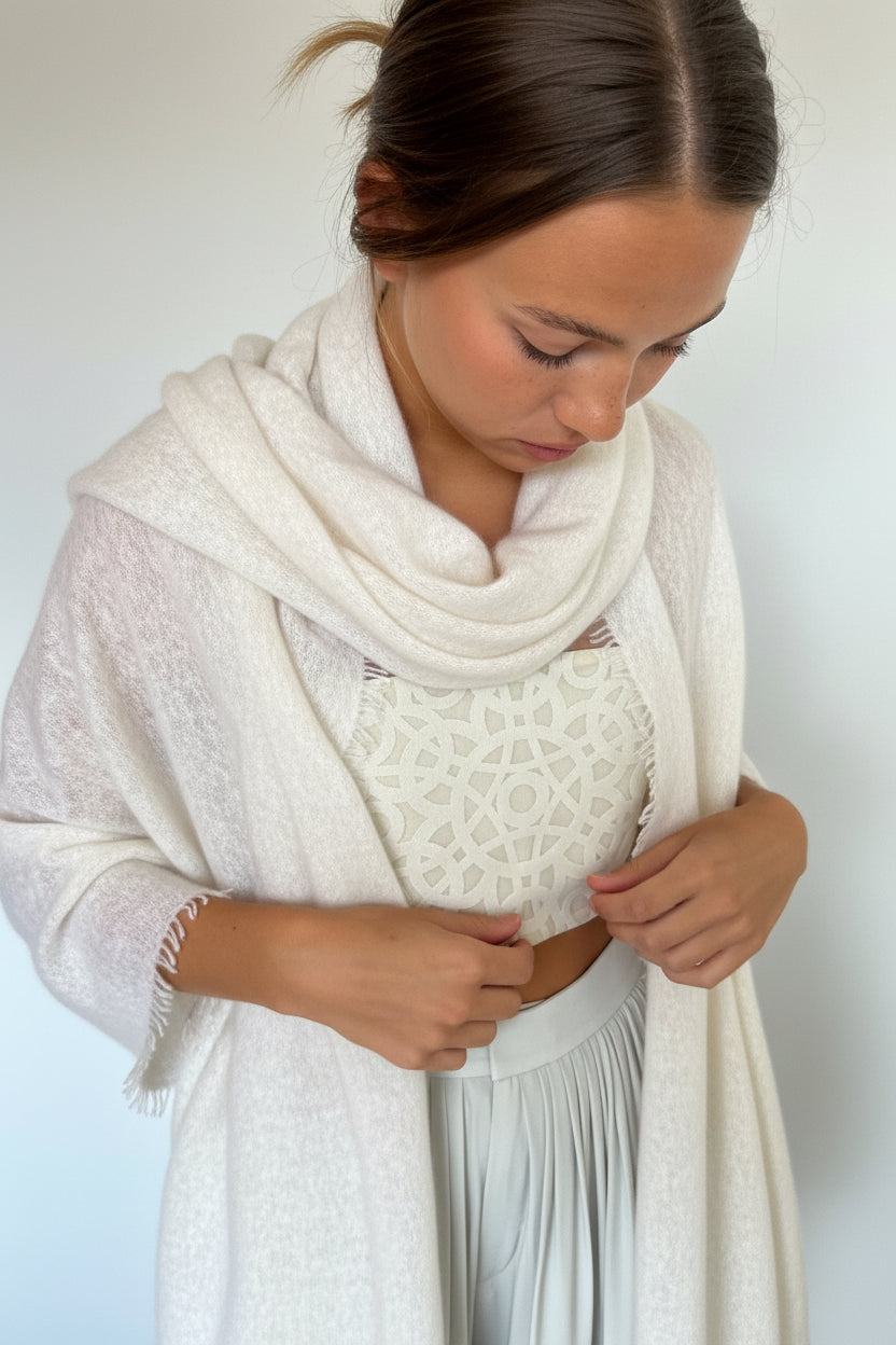 A woman wearing a white textured knit cardigan with frayed edges over a white patterned top and light gray skirt, posed against a plain white wall.