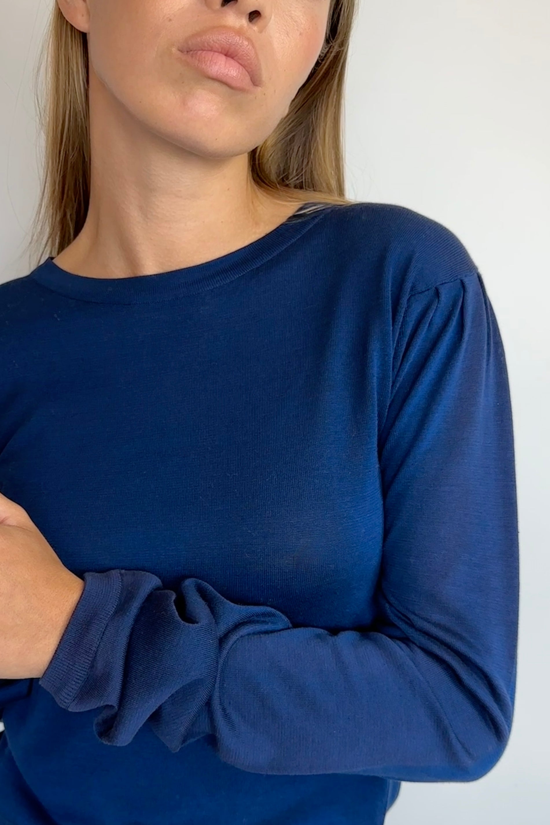 A close-up of a woman wearing a solid navy blue long-sleeve top, showing the fabric texture and fit against a plain light background.