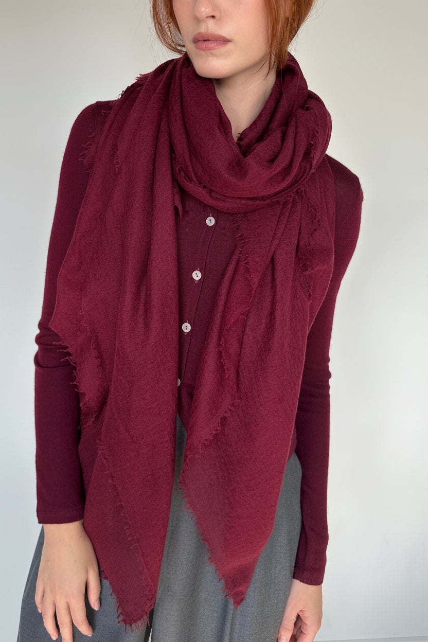 A person wearing a large, deep burgundy scarf draped over a matching burgundy button-up top and gray skirt, photographed against a plain light gray background.