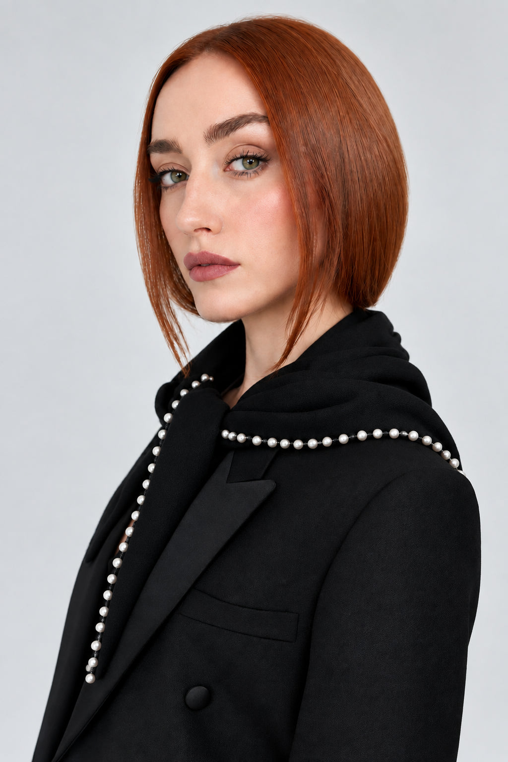 A woman with short red hair is shown in profile wearing a black double-breasted blazer with black satin lapels and silver stud embellishments along the collar.