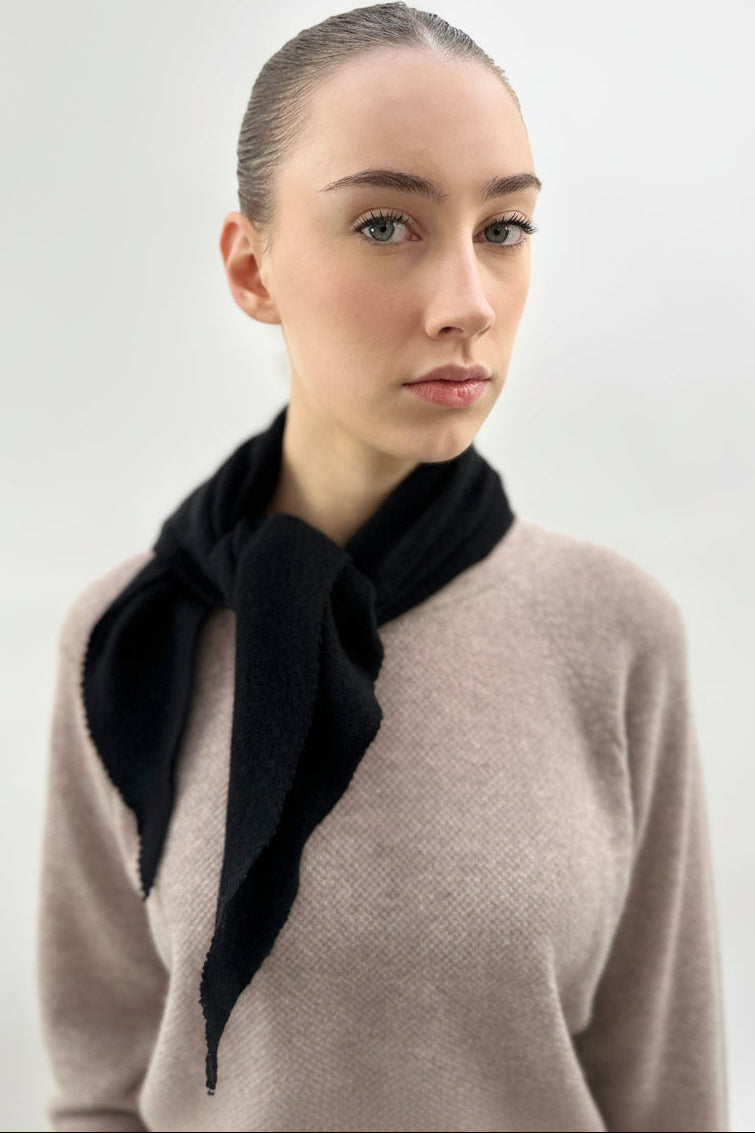 Woman wearing a black scarf and beige sweater against a plain background