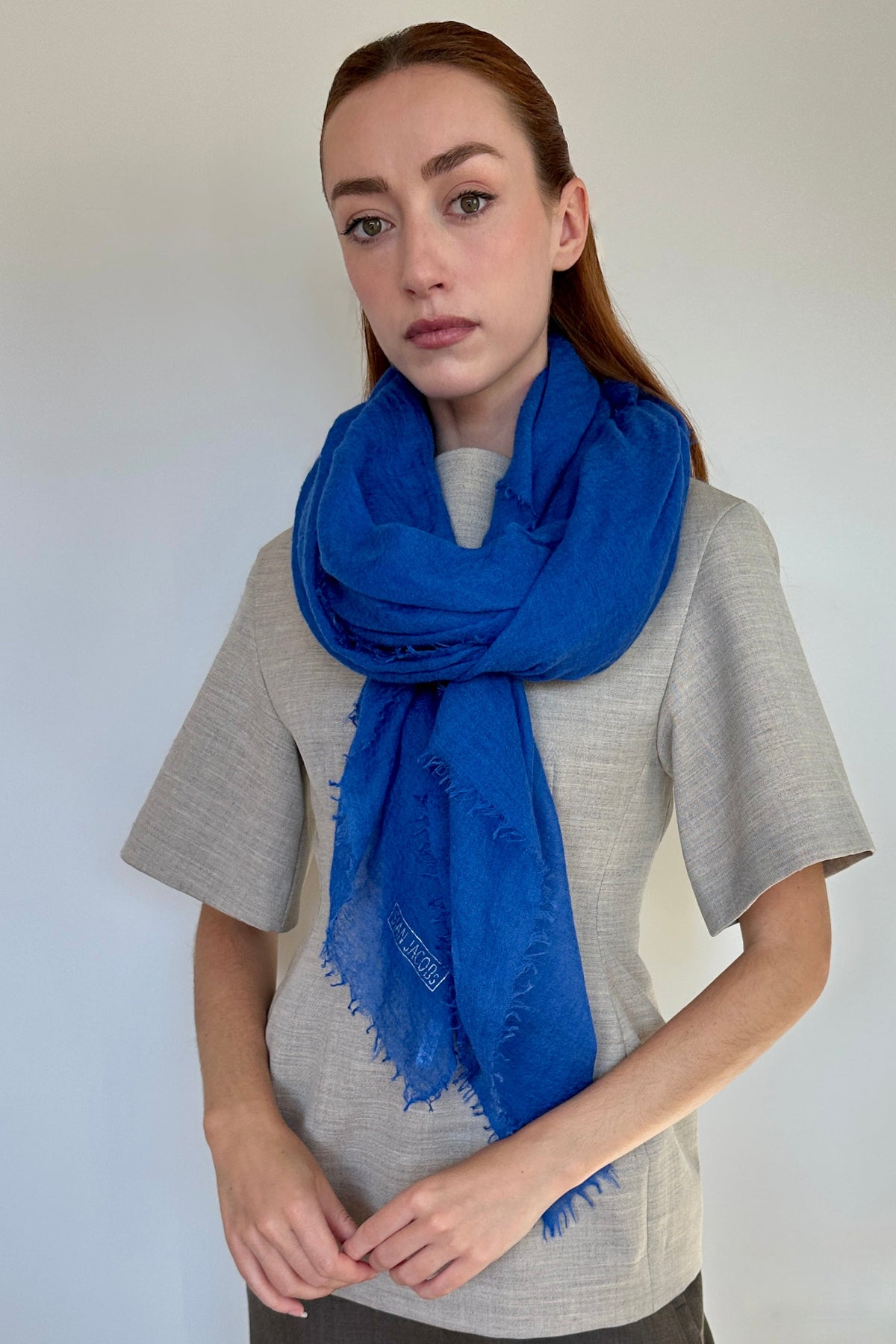 A woman modeling a vibrant royal blue cashmere scarf with fringed edges, wrapped around her neck over a light gray linen shirt.