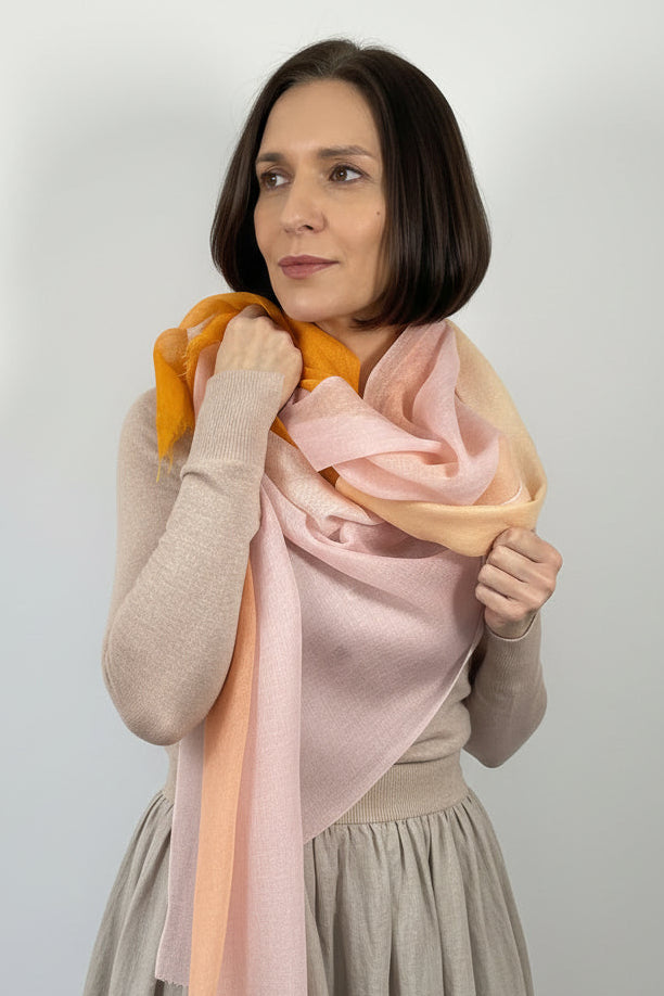 Woman adjusting a pink scarf around her neck against a plain background