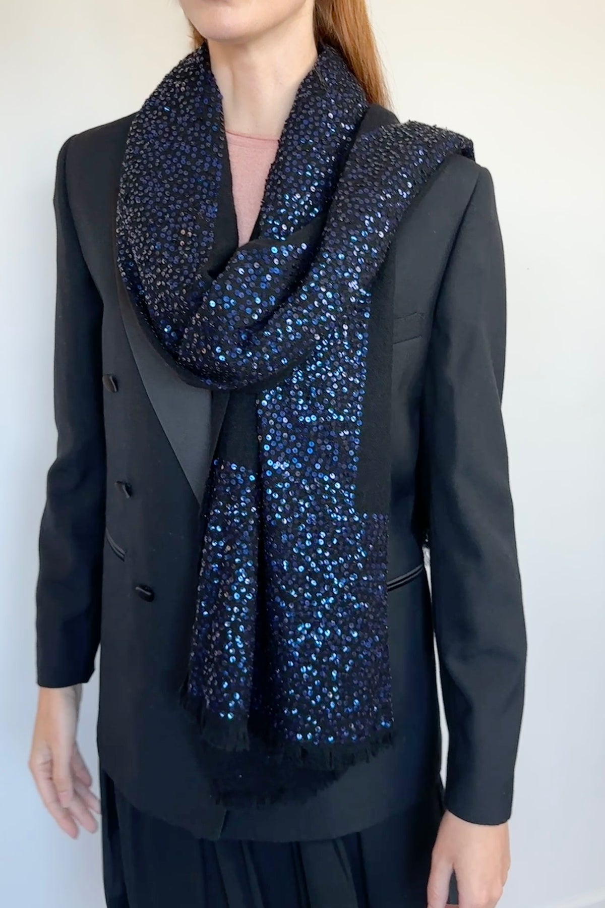 A model wearing a black double-breasted blazer and a black base with dark blue sequined cashmere scarf with fringe.