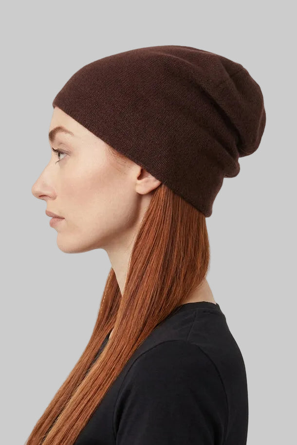 A woman with long auburn hair is shown in profile wearing a dark brown cashmere knit beanie and a black short-sleeve top against a plain light gray background.