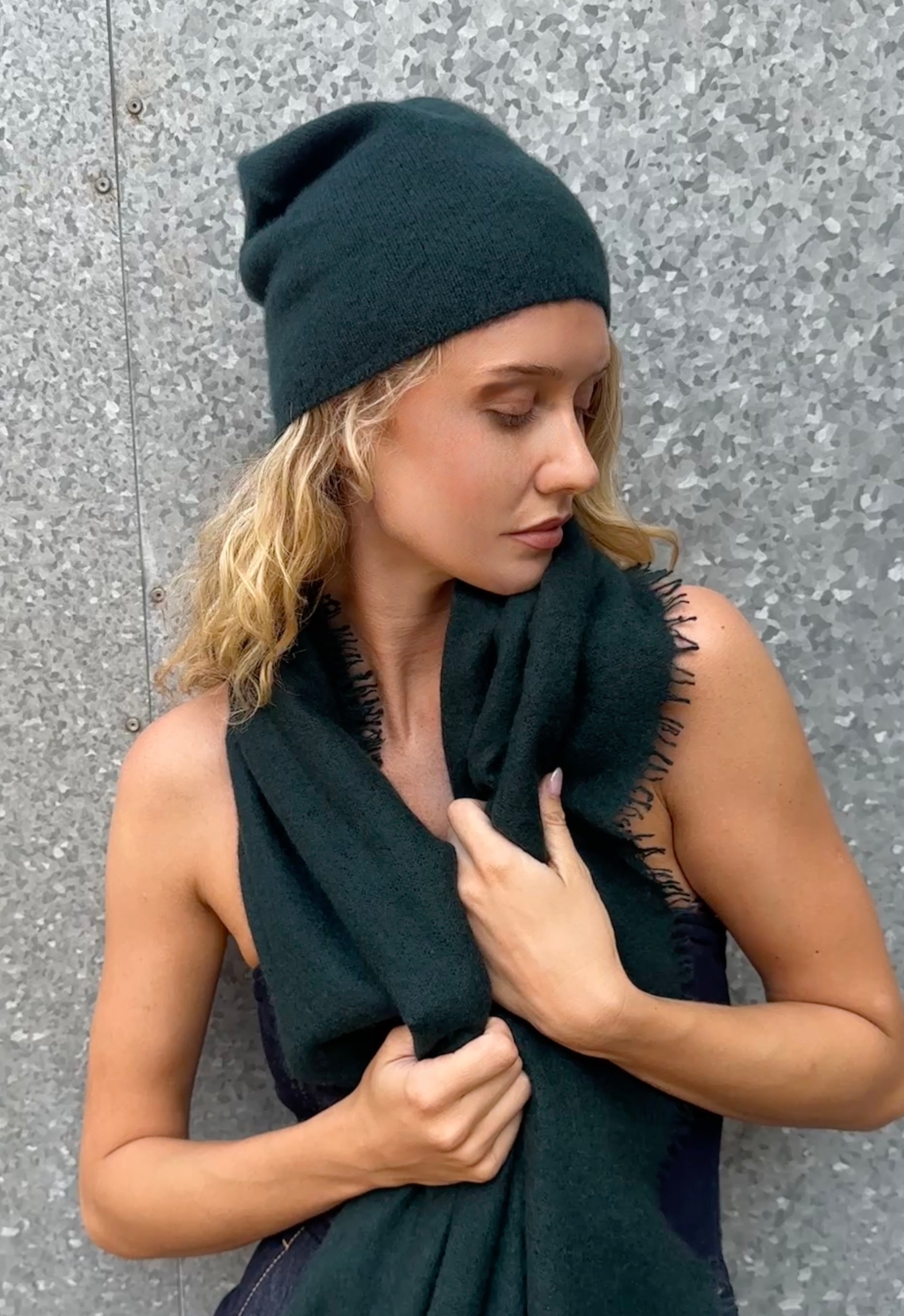 Model wearing a bottle green cashmere beanie and scarf against a gray wall