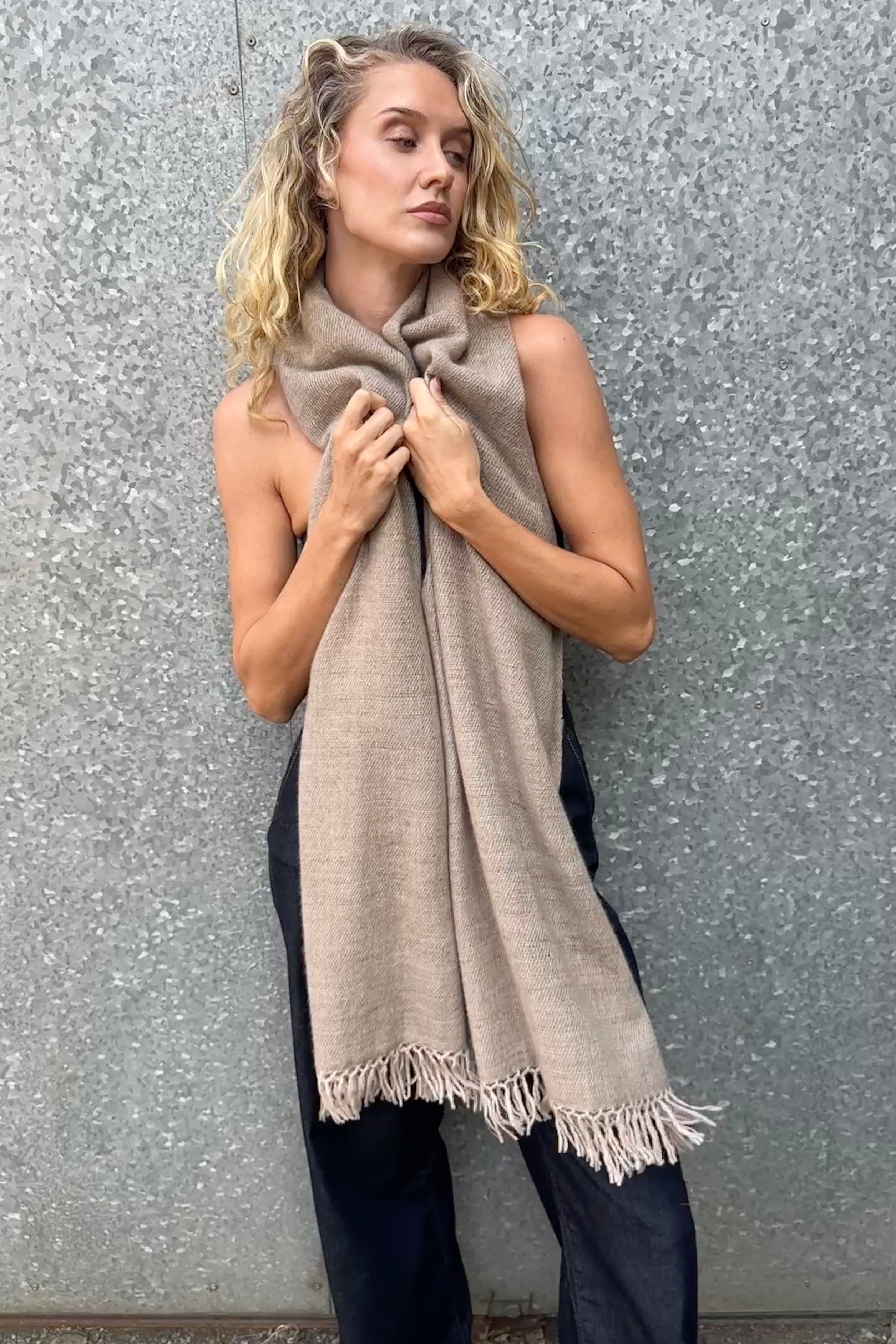 model wearing a beige cashmere blanket  shawl with fringes against a gray background