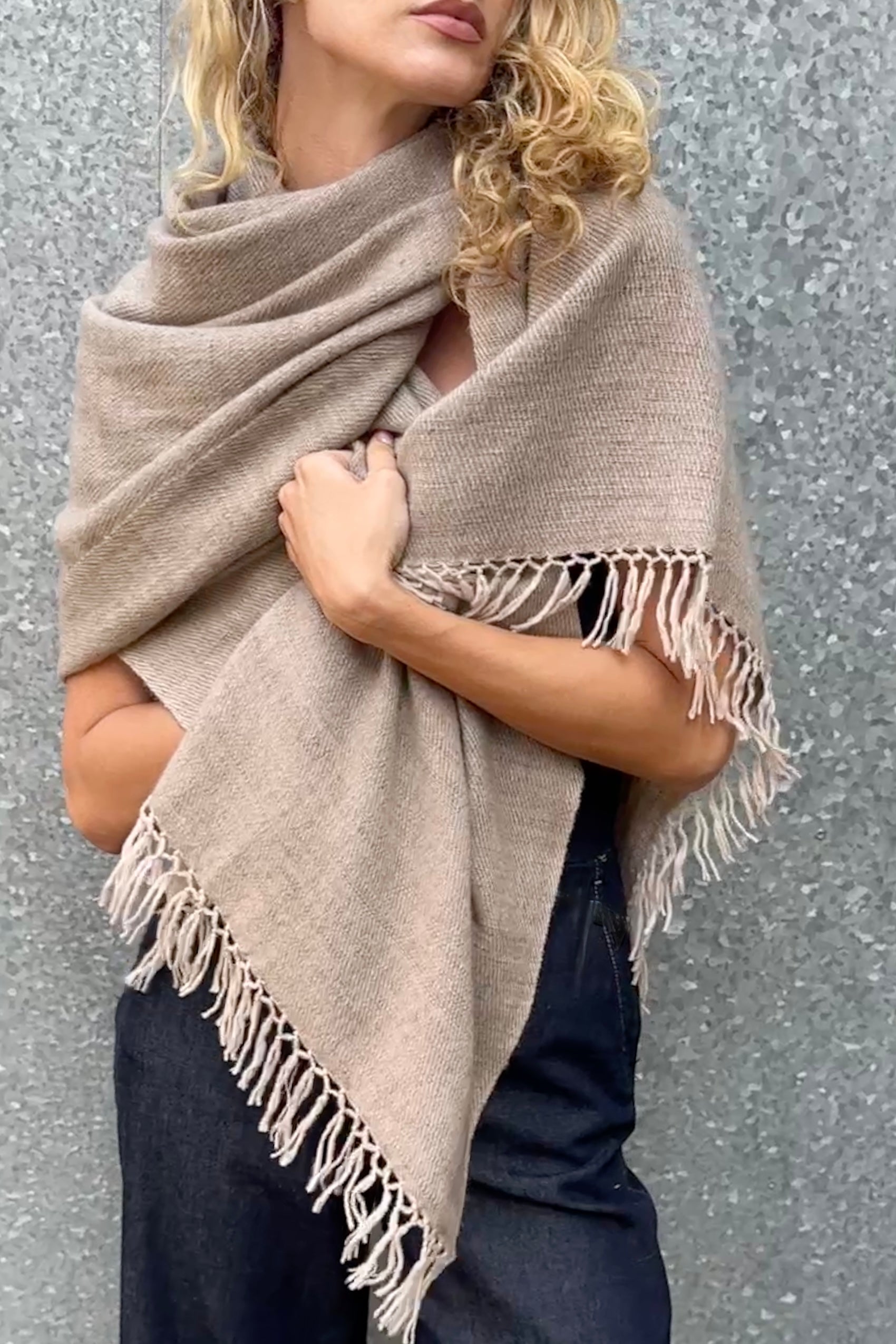 model wearing a beige cashmere blanket  shawl with fringes against a gray background