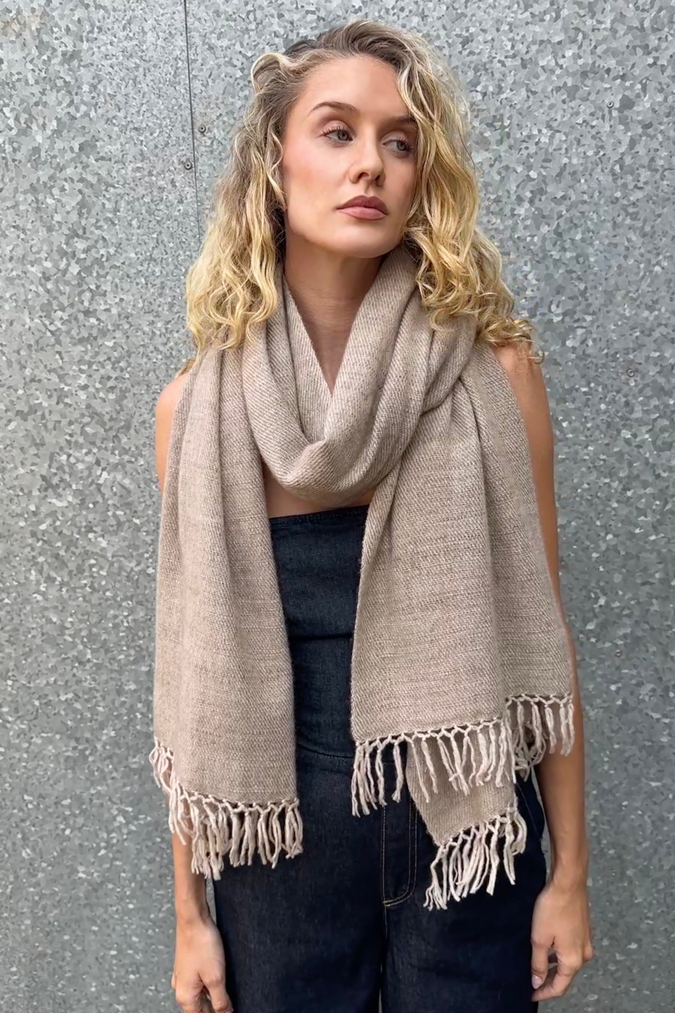 model wearing a beige cashmere blanket  shawl with fringes against a gray background