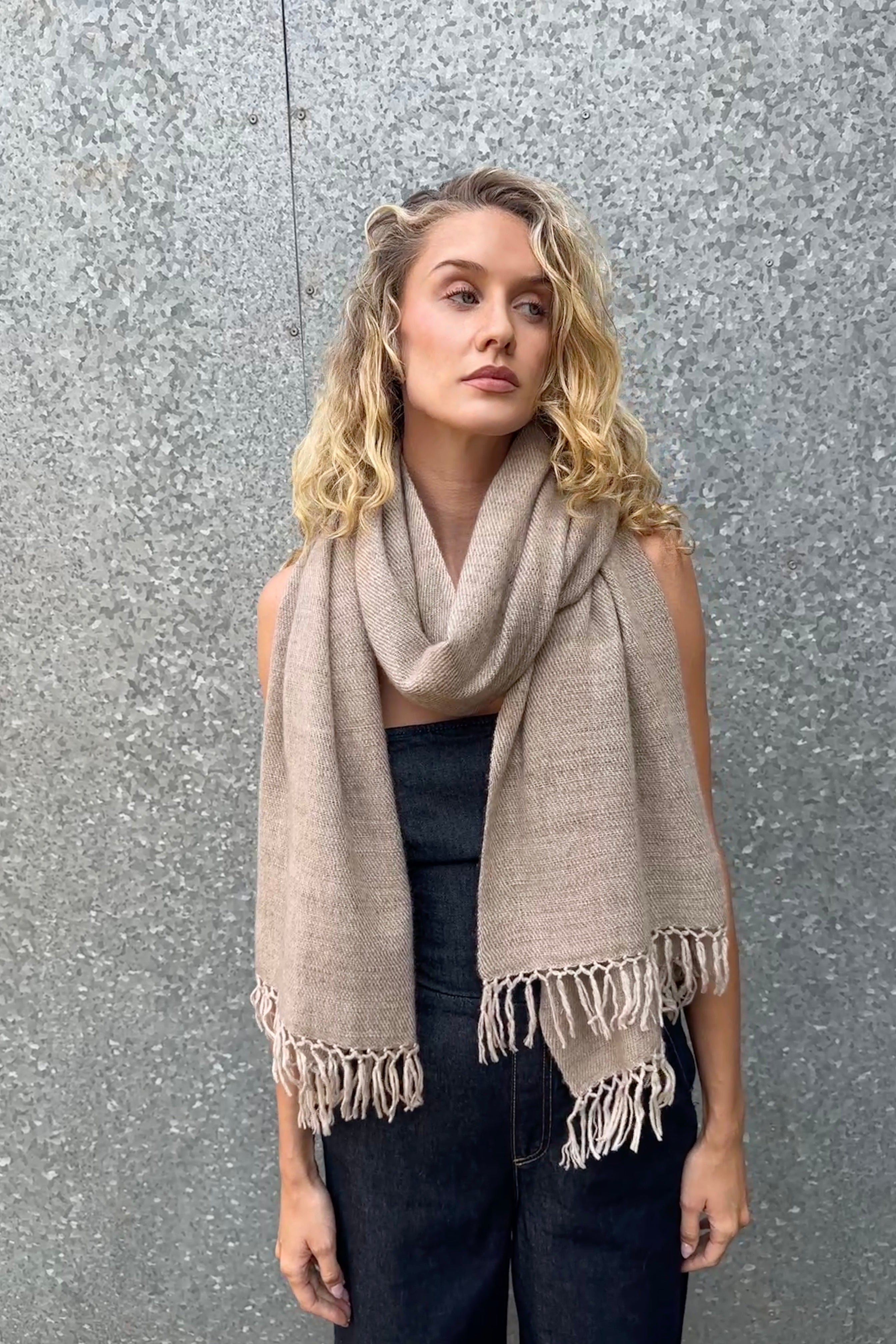model wearing a beige cashmere blanket  shawl with fringes against a gray background