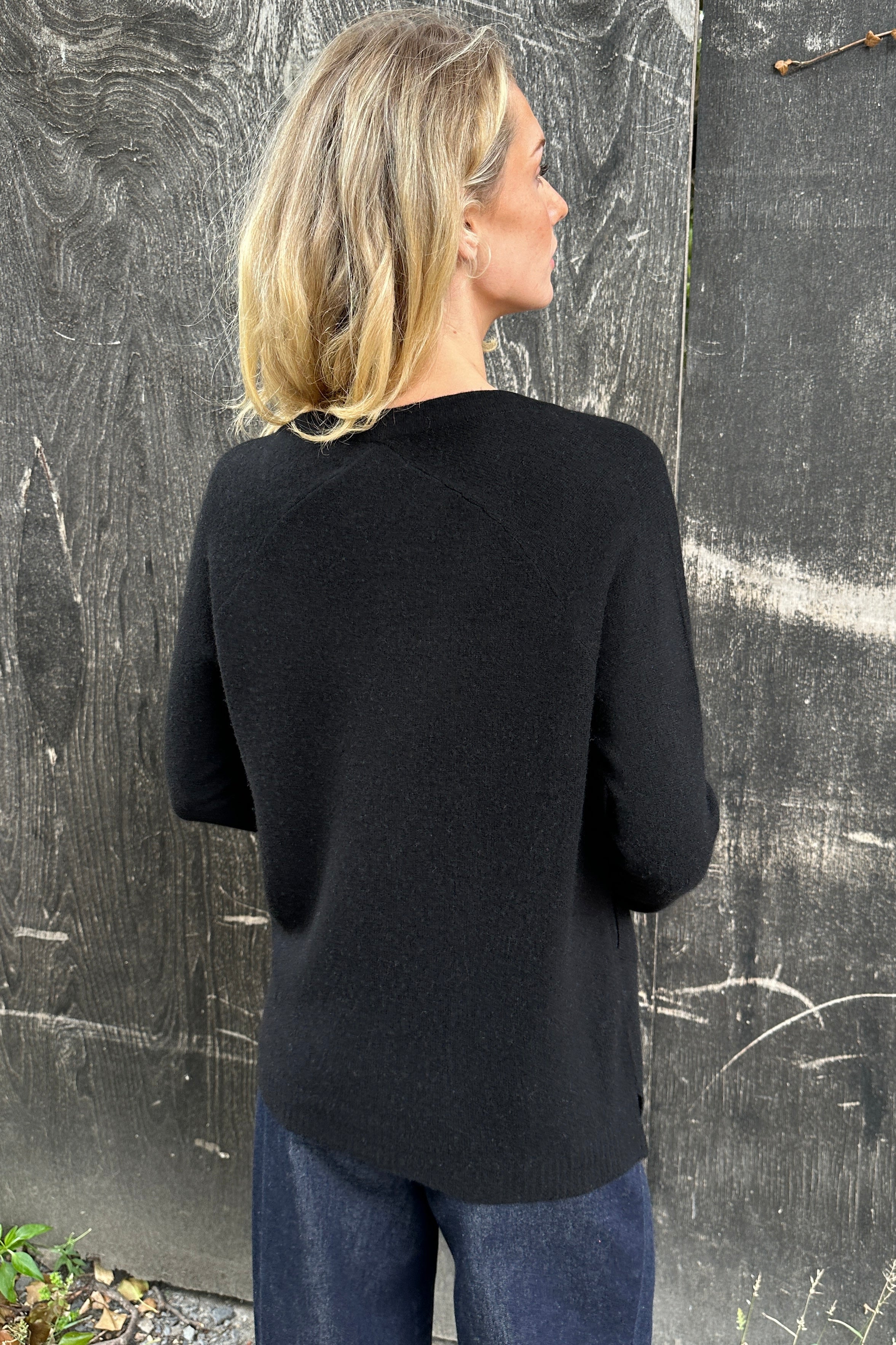 Woman wearing a black cashmere zola cardigan against a textured gray  back view