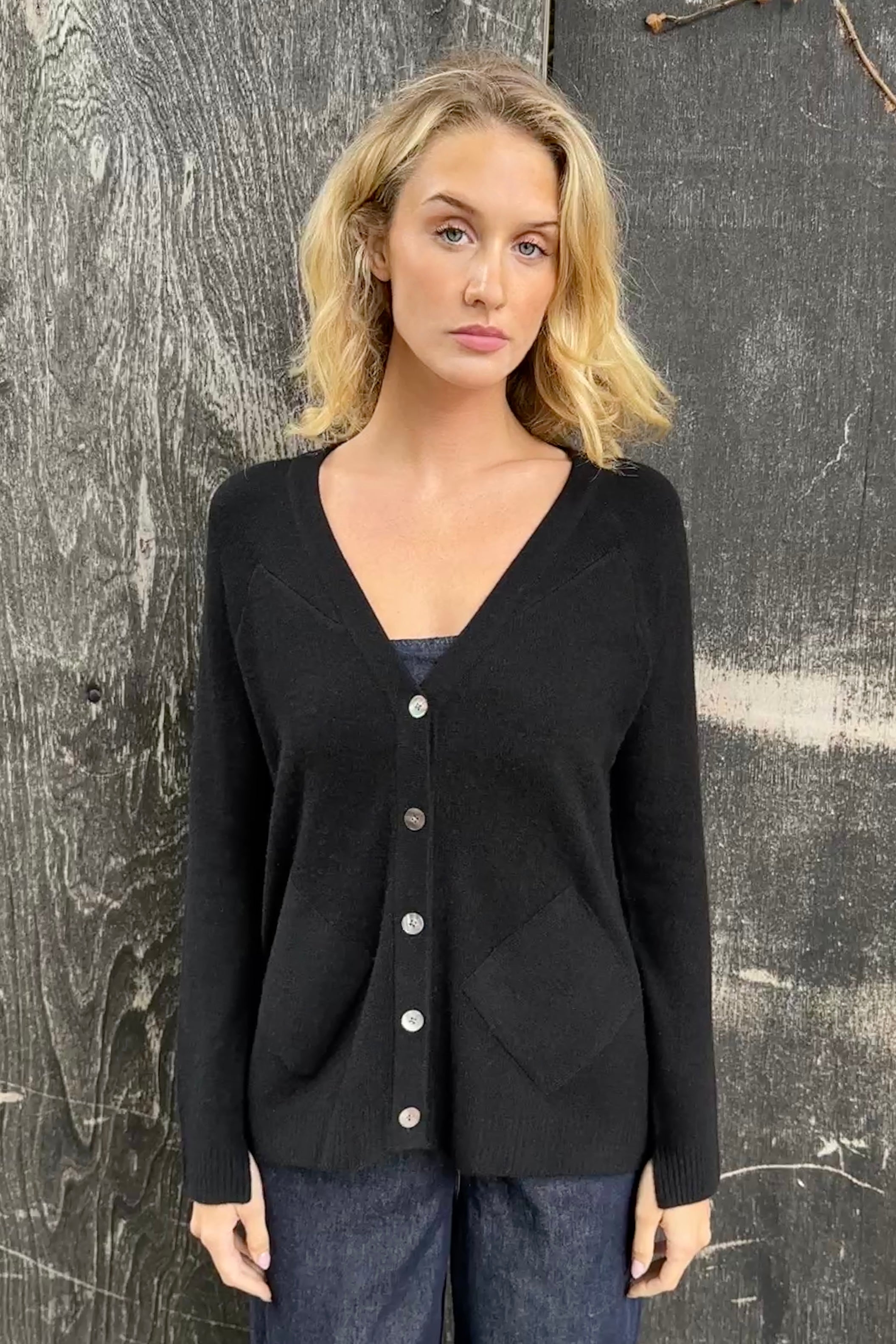 Woman wearing a black cashmere zola cardigan against a textured gray 