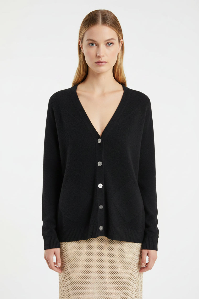 Woman wearing a black cashmere zola cardigan against a textured gray 