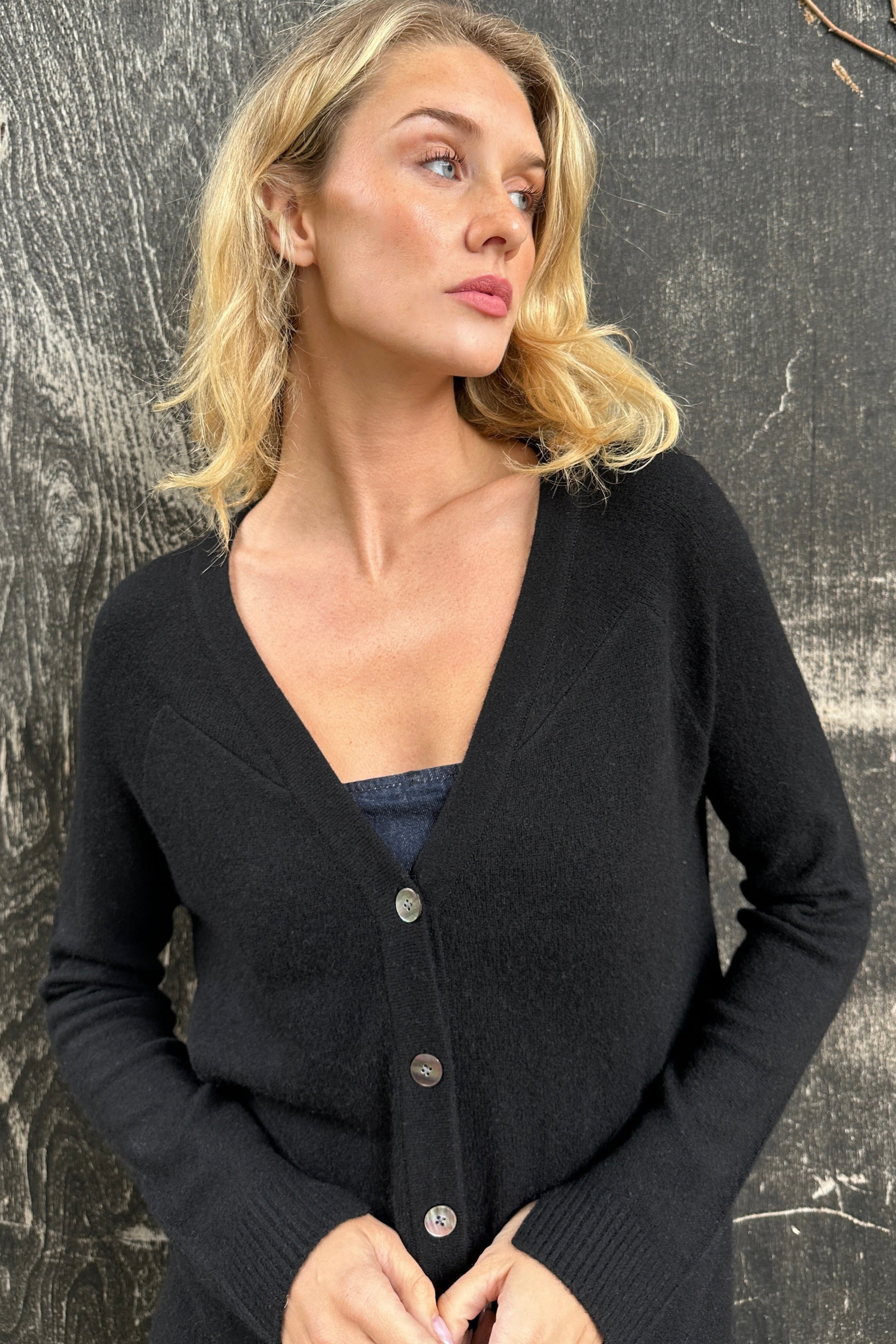 Woman wearing a black cashmere zola cardigan against a textured gray  close up 