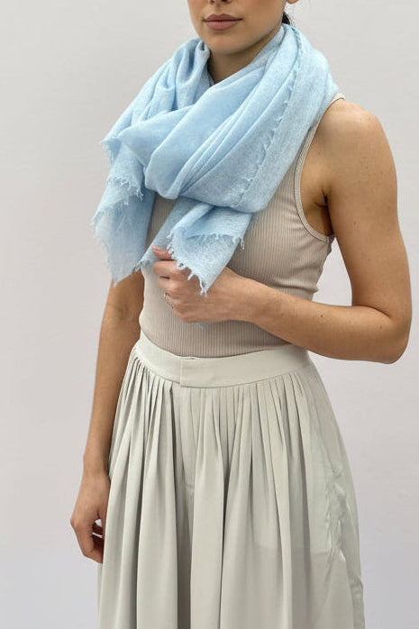 Woman wearing a light blue scarf and silver dress in a room with a white wall.