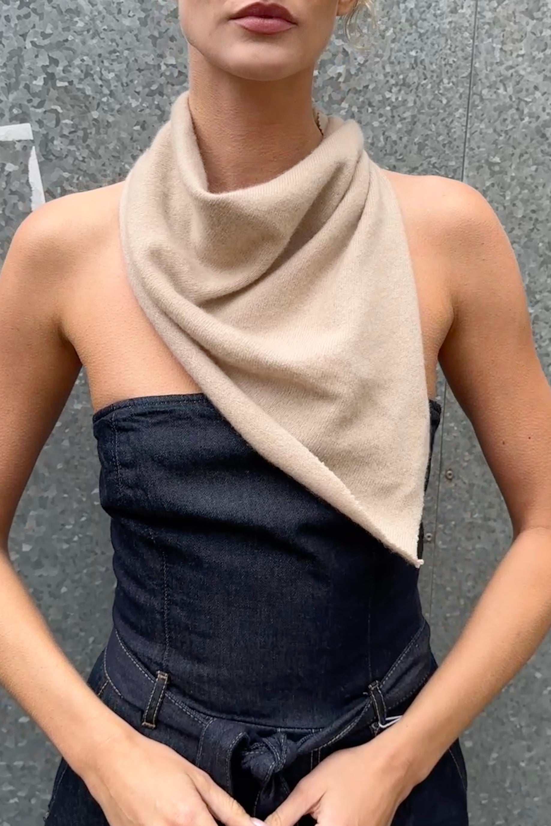 Person wearing a beige doon cashmere scarf over a black strapless top against a gray background