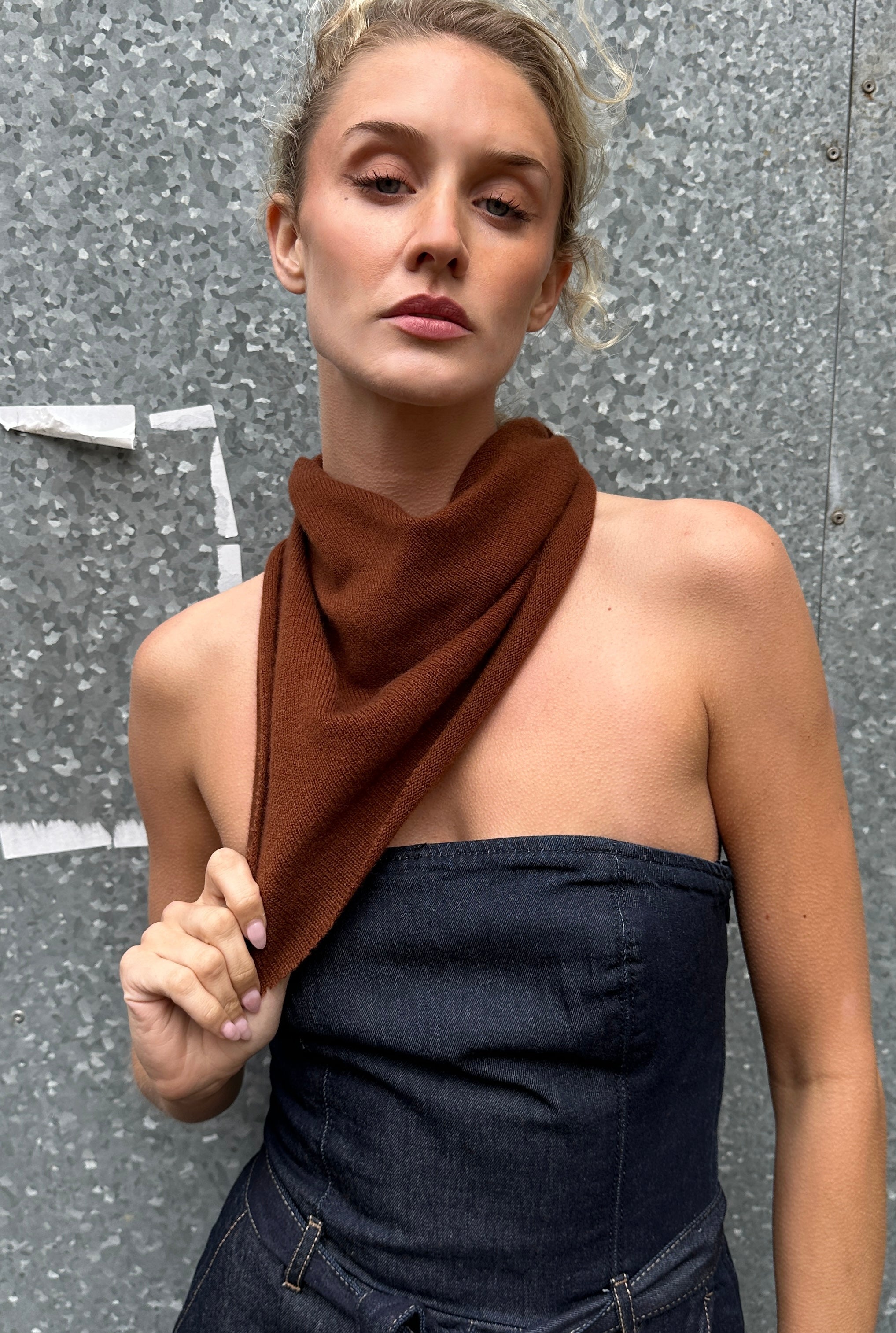 Woman wearing a brown  doon cashmere scarf and dark blue strapless top against a textured wall.