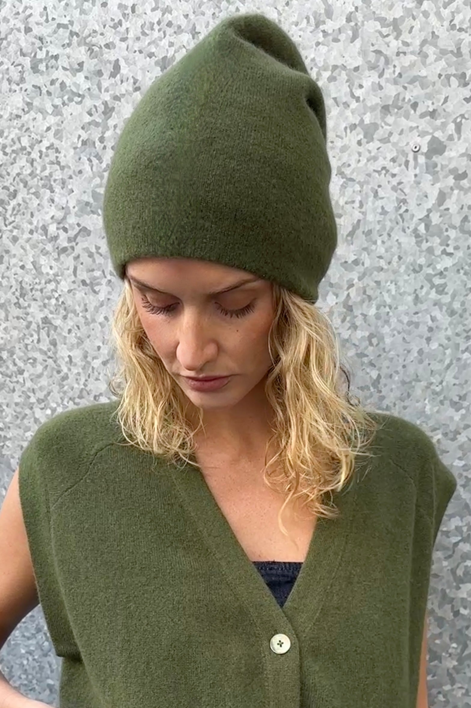 model wearing a revo  green knitted hat and vest against a textured gray background