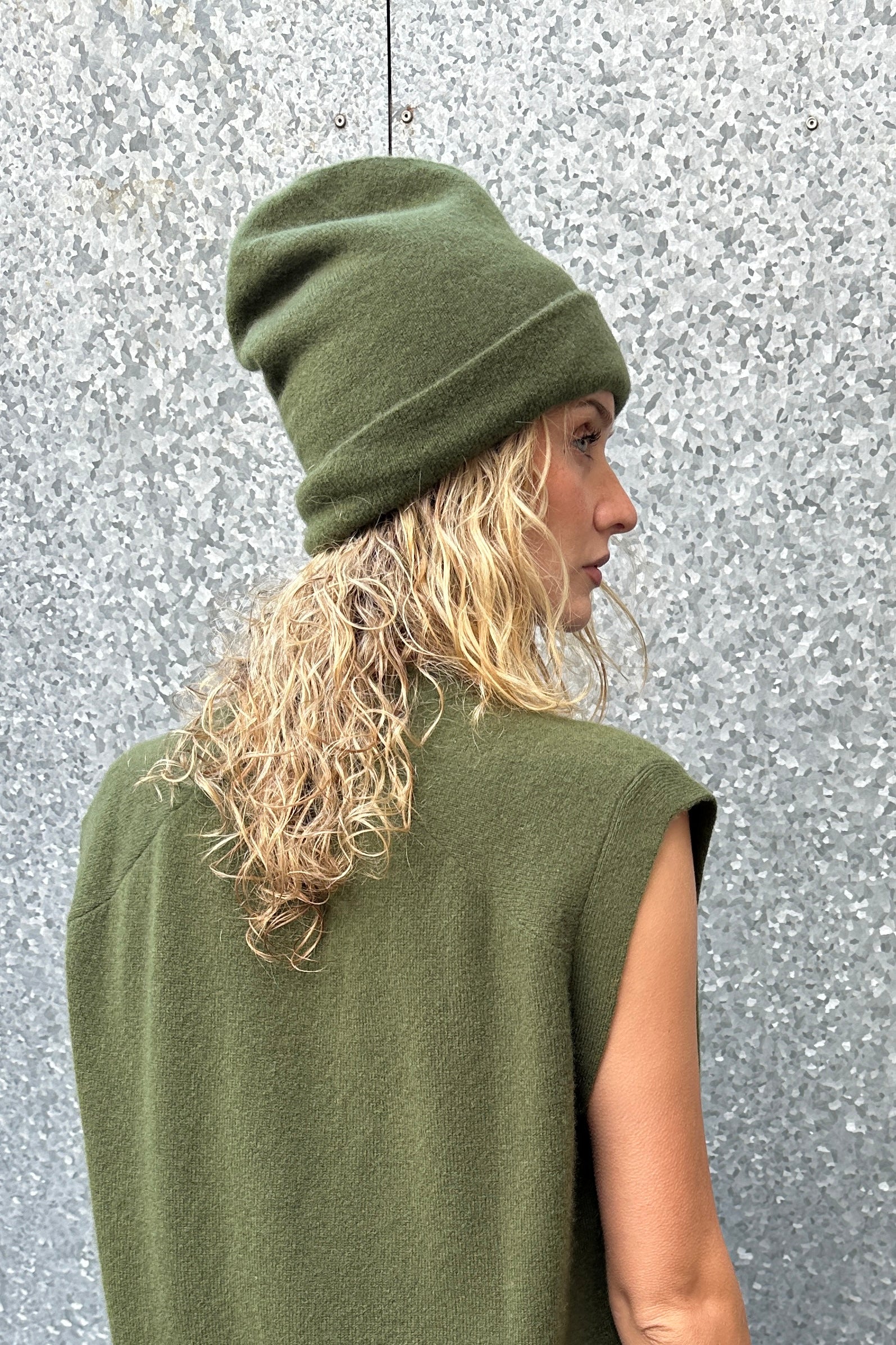 Person wearing a green beanie and sleeveless top against a textured gray background