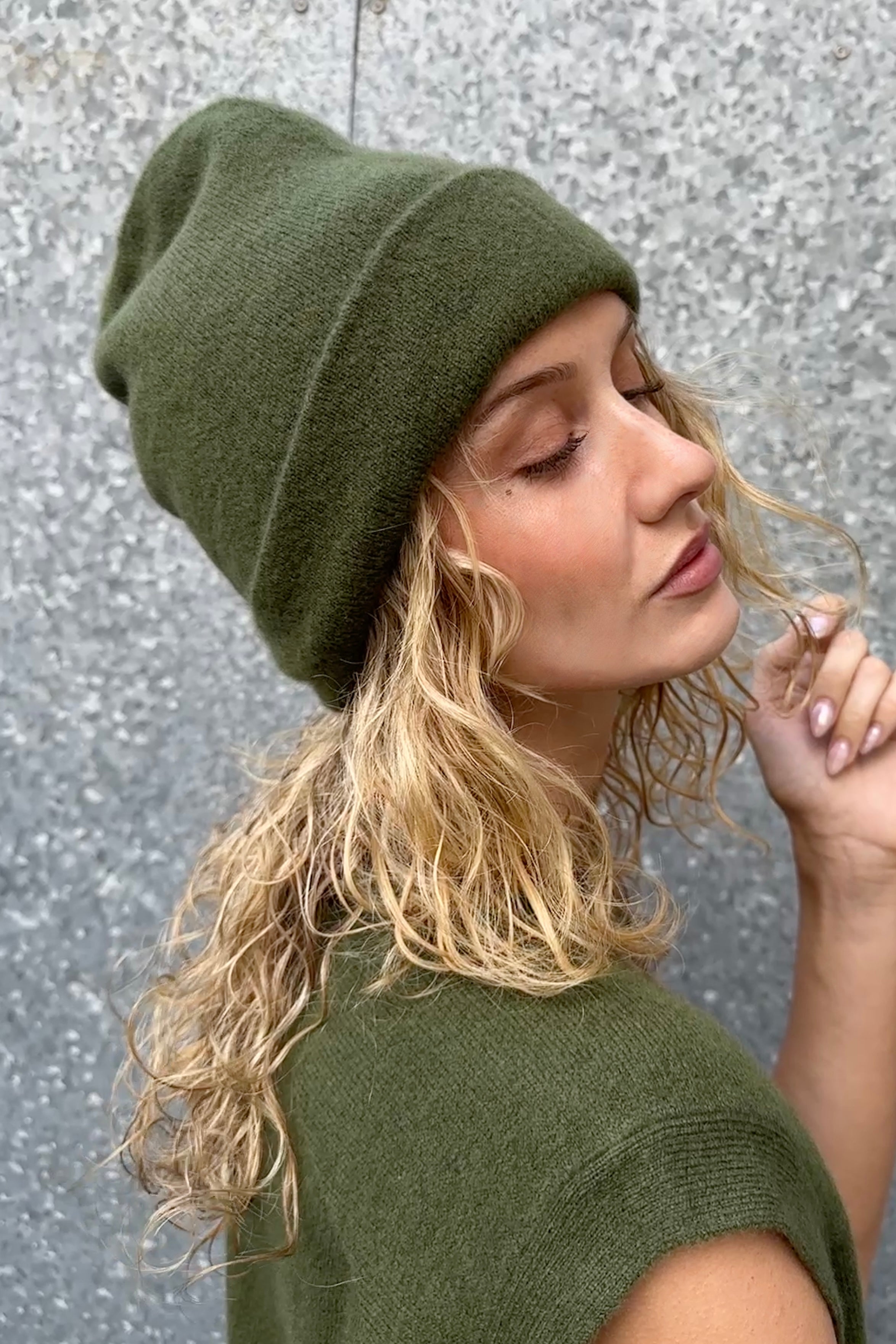 Woman wearing a green beanie and matching outfit against a textured wall.