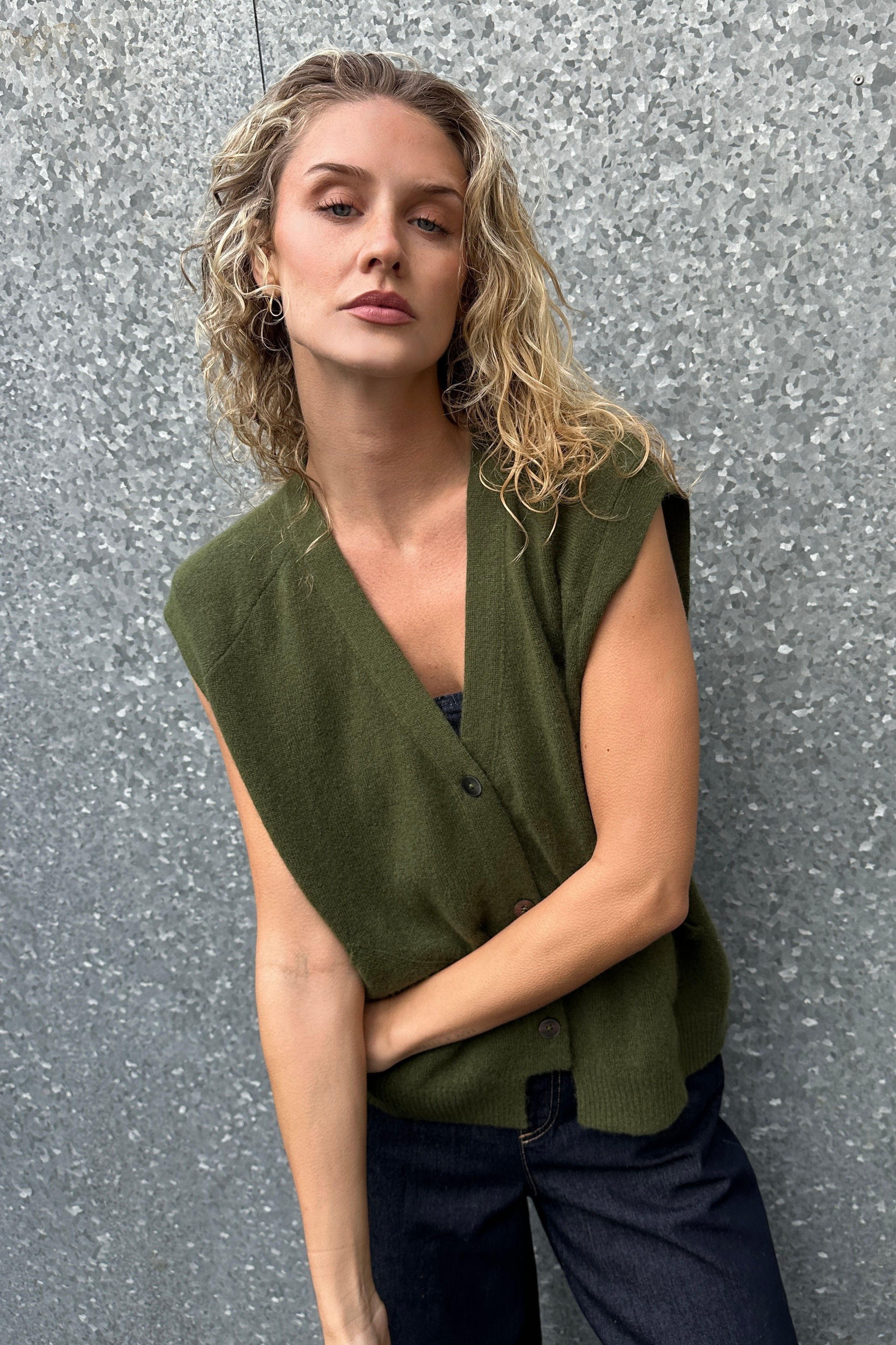 Woman wearing a olive  green vest against a textured gray wall