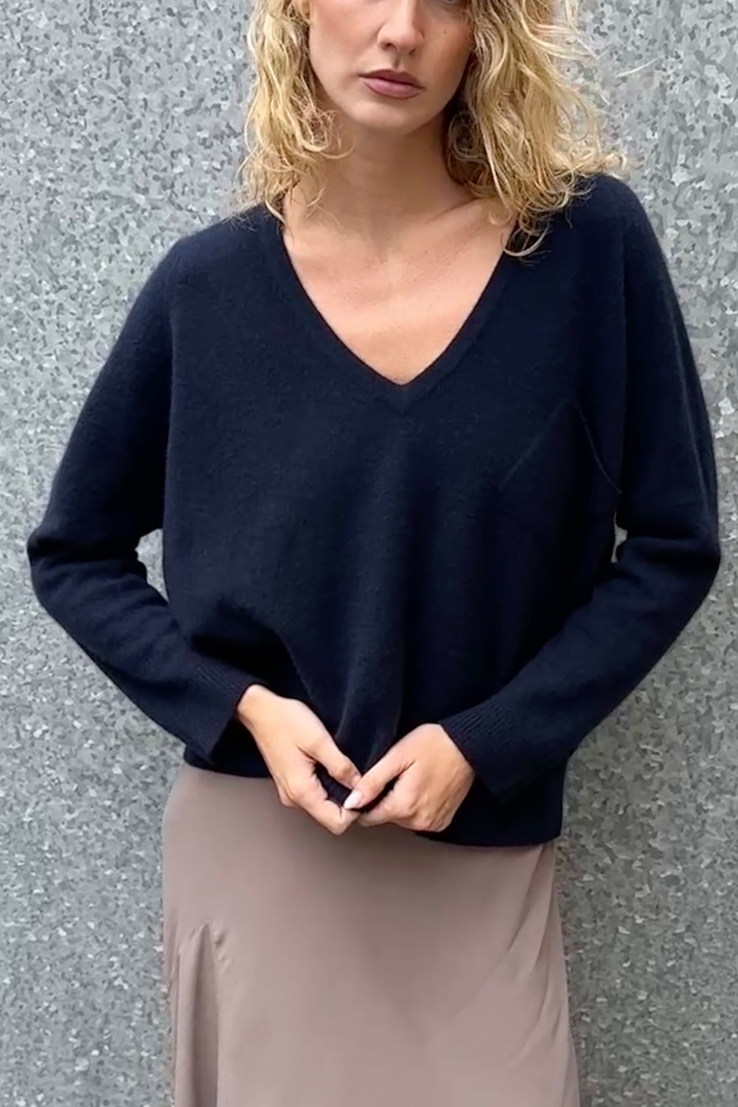 Woman wearing a navy blue v neck sweater against a gray background