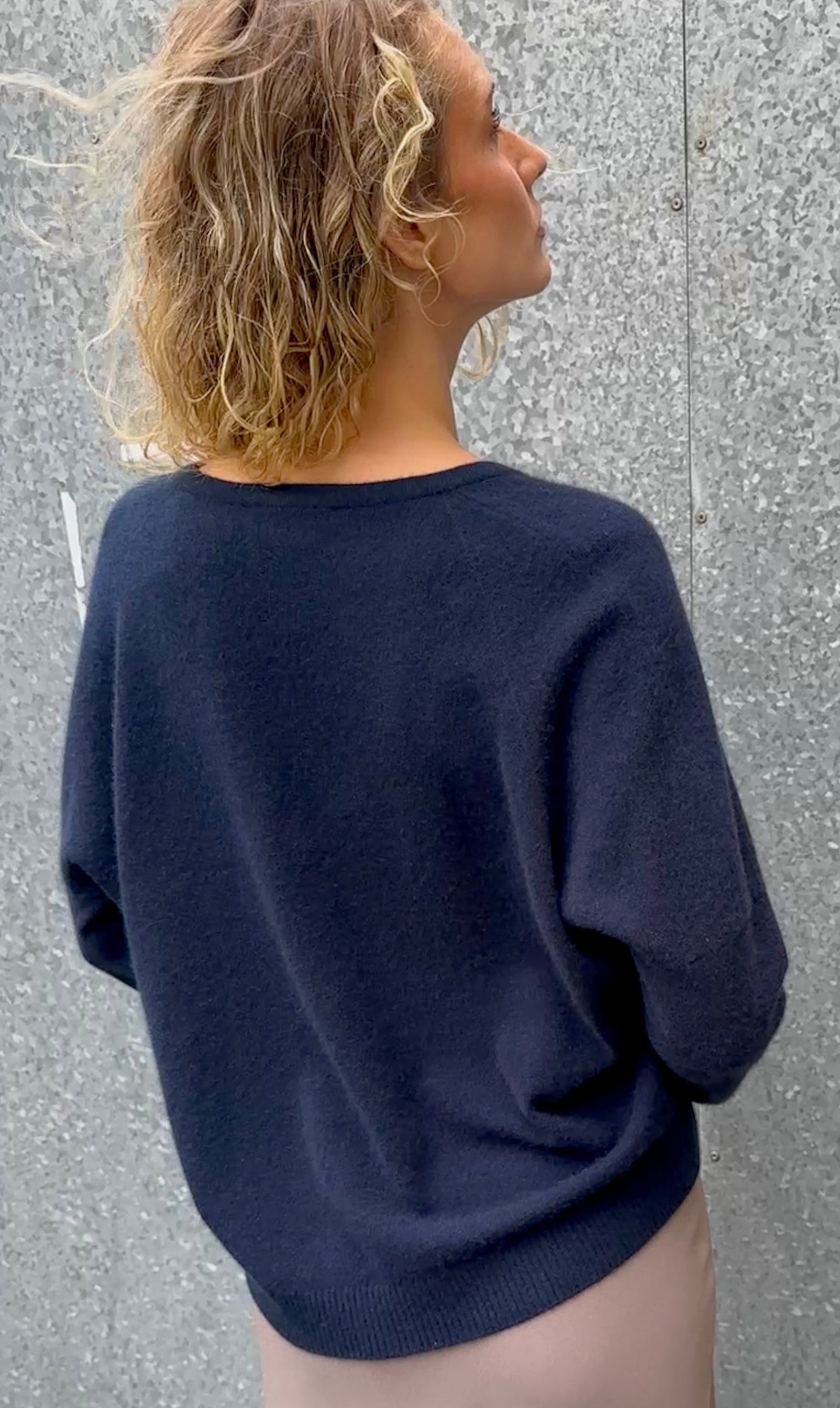 Person wearing a navy blue v  sweater against a textured gray wal