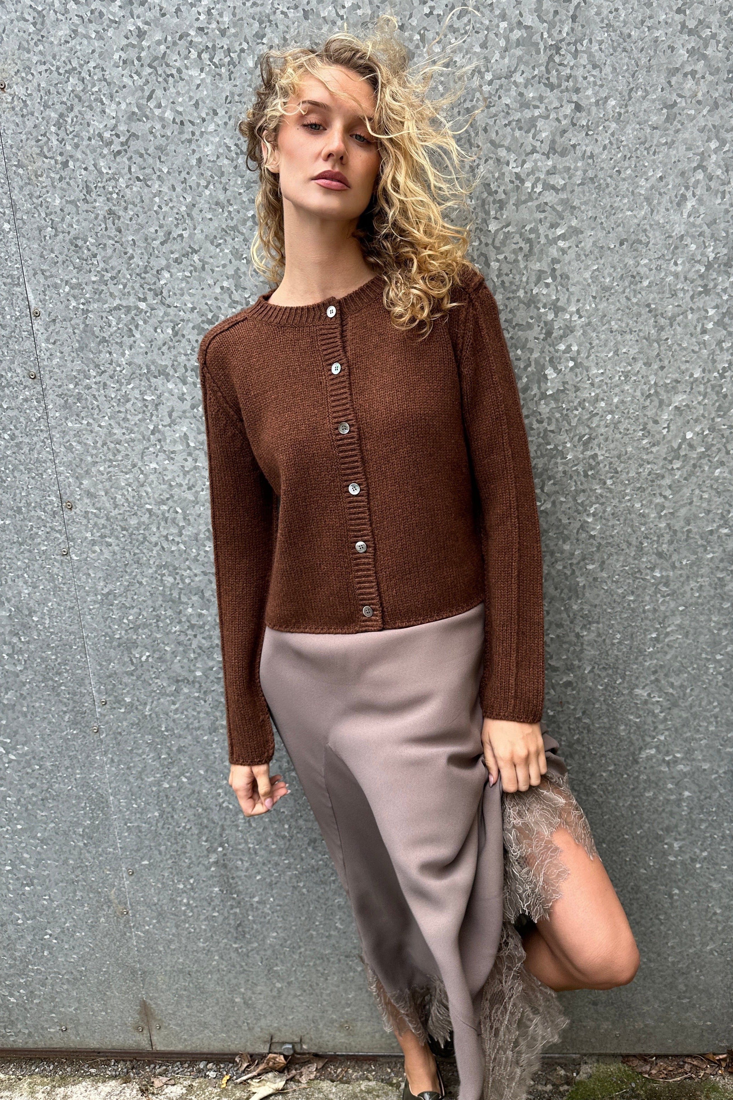 Woman wearing a brown cardigan and beige skirt against a gray wall
