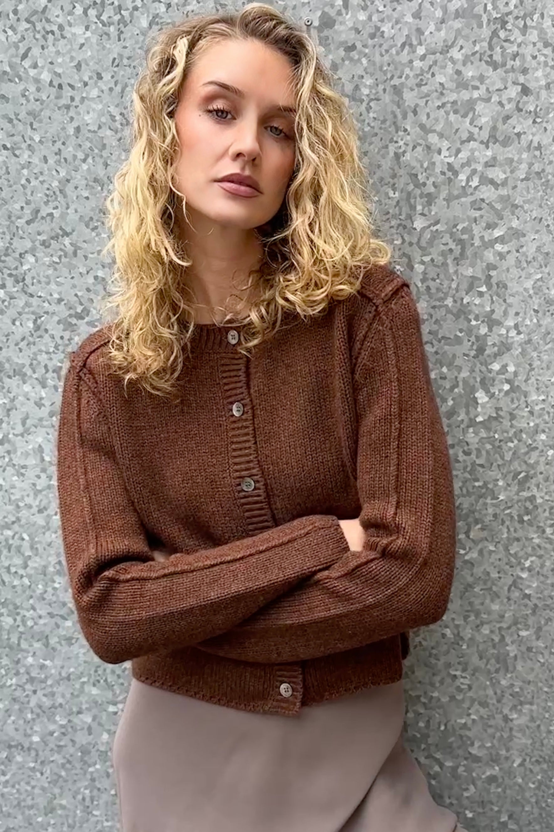 Woman wearing a brown knitted cardigan against a gray background