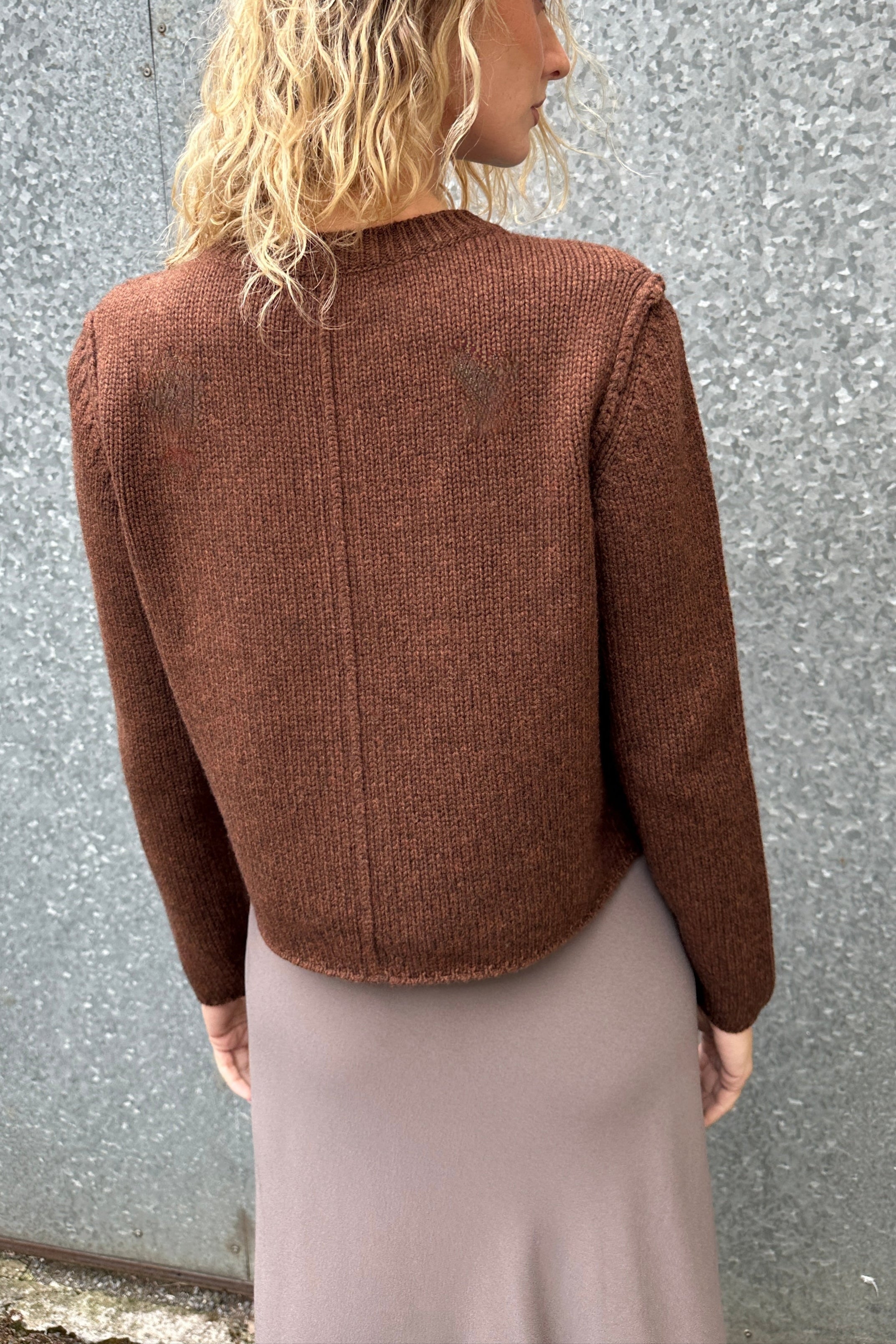 Person wearing a brown cardi back view against a gray wall