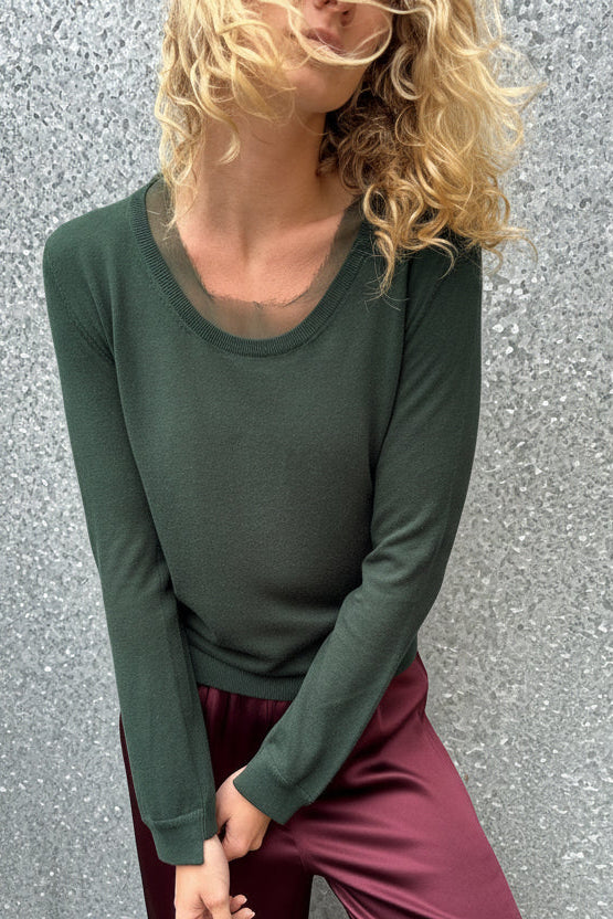 Person wearing a green long-sleeve top and maroon pants on a gray wall