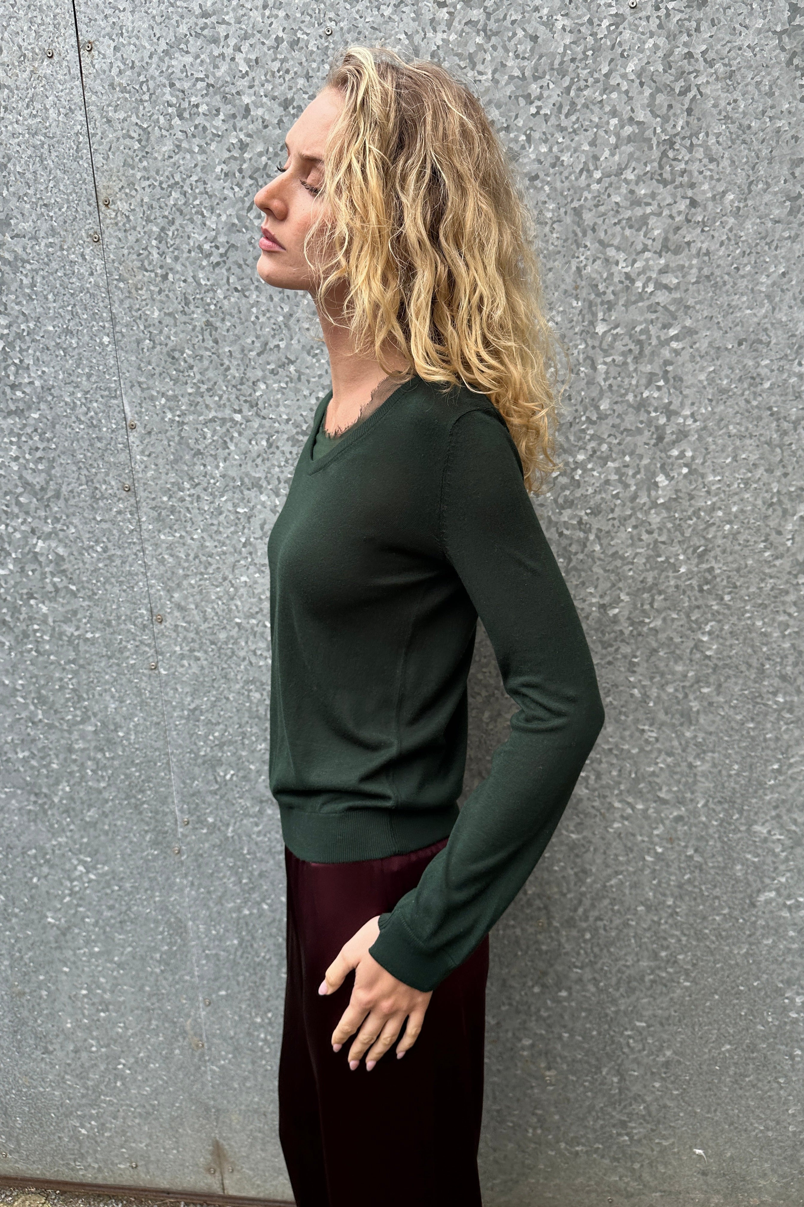 Person wearing a green long-sleeve shirt and maroon pants on a gray pavement.