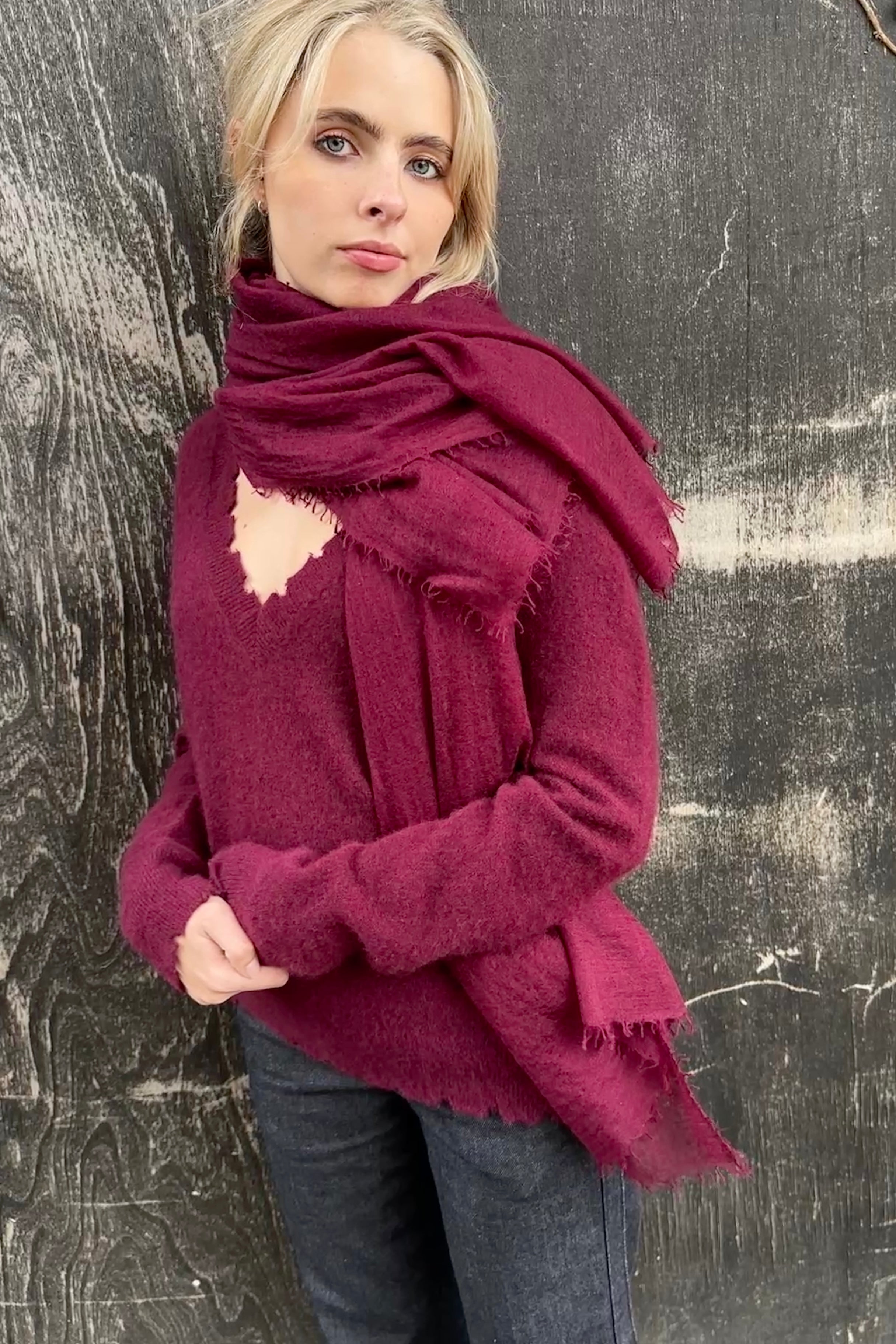 Woman wearing a large burgundy cashmere marmee scarf against a textured gray background